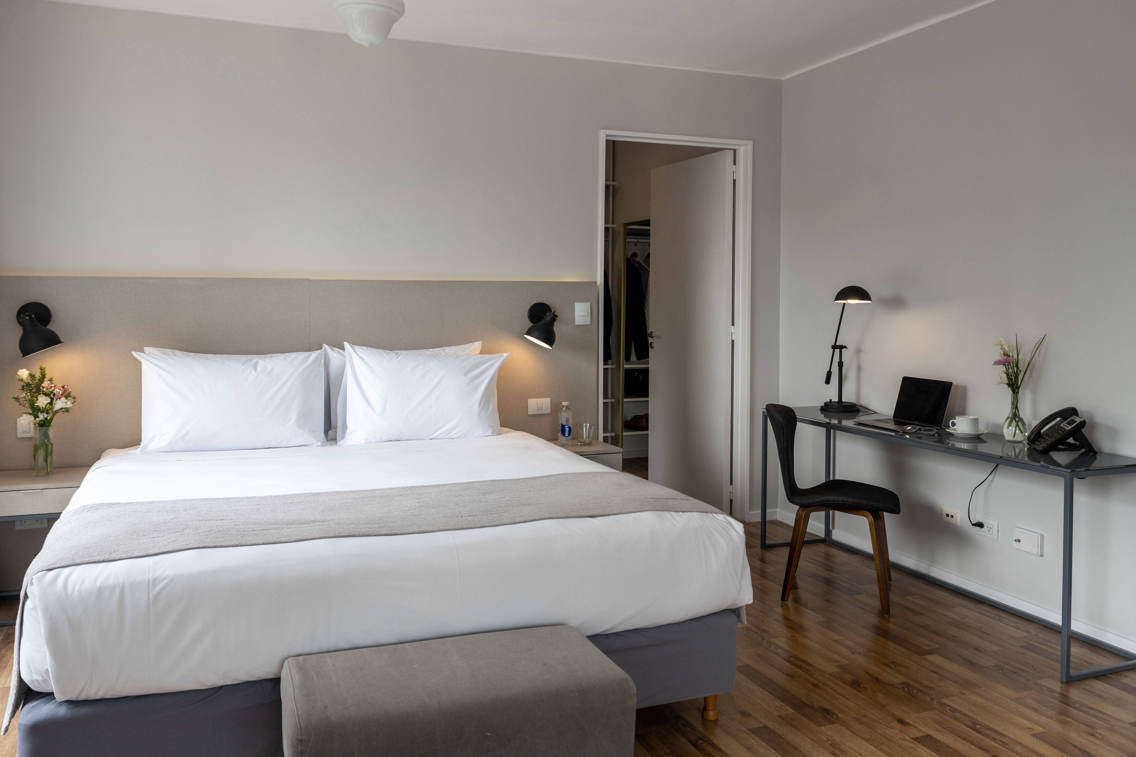 Bright hotel bedroom with large bed, grey headboard, and desk workstation.