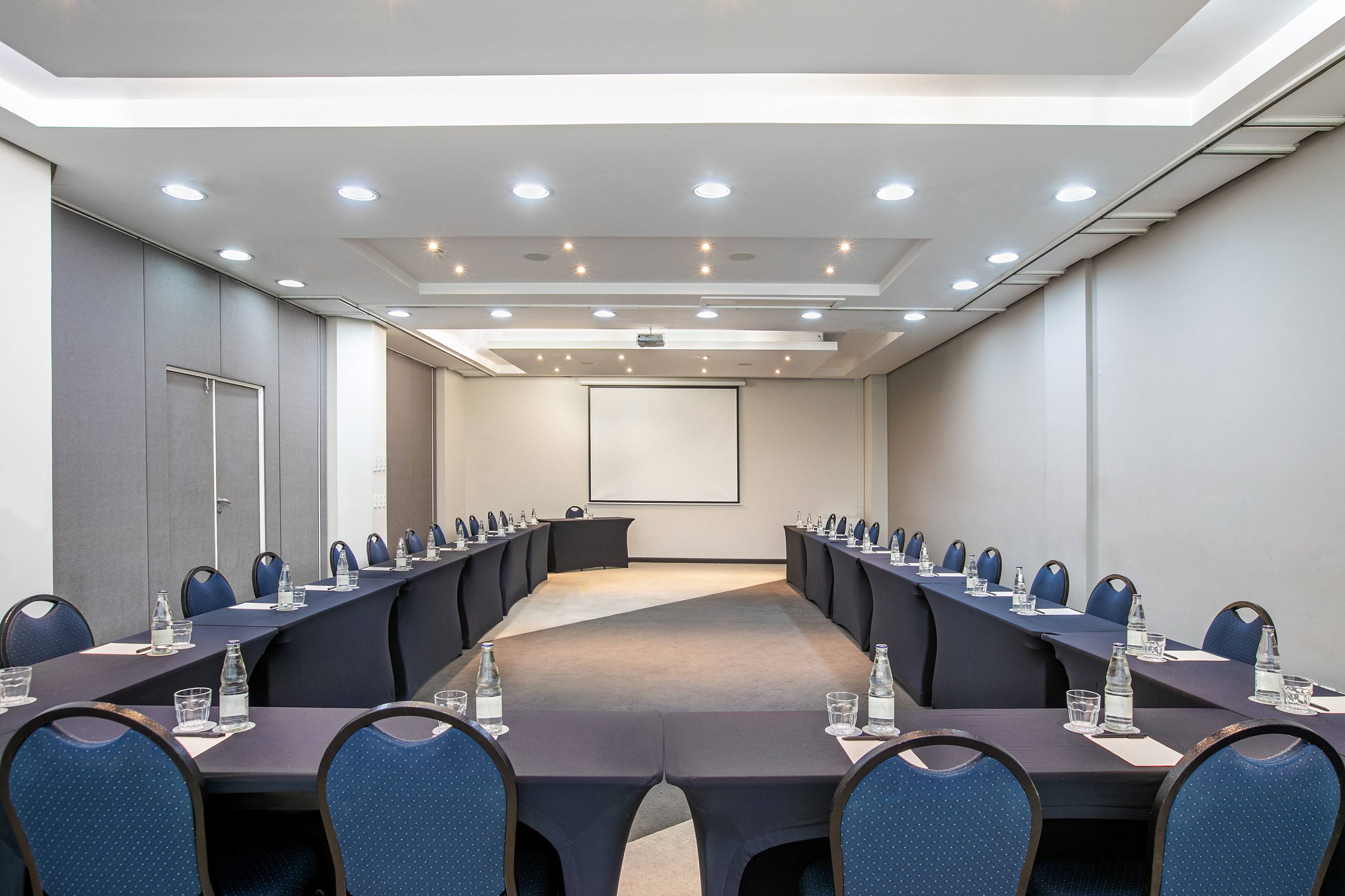 Modern U-shaped conference room with projector screen and blue chairs.