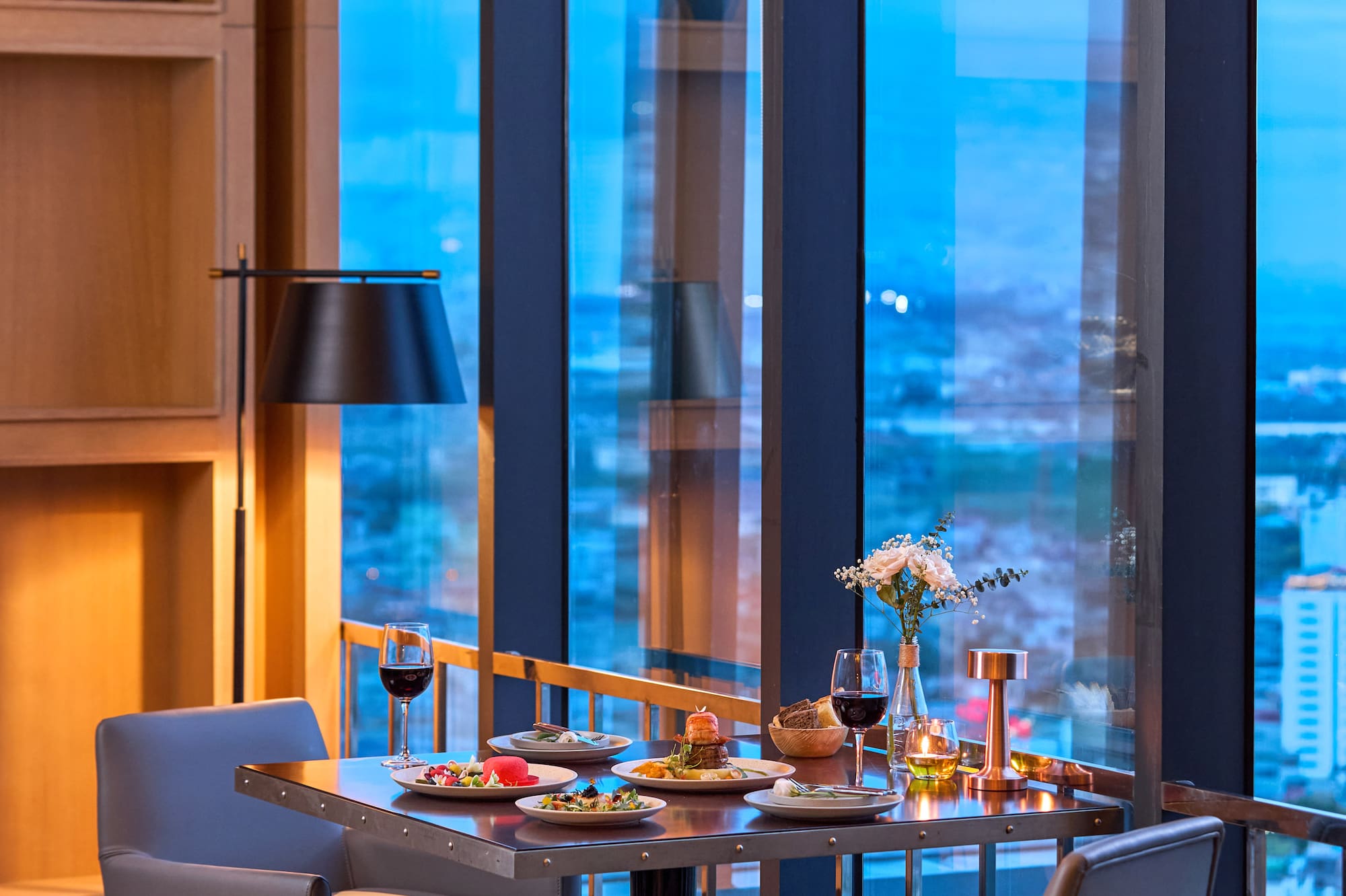 Elegant dinner table for two with food, wine, and evening city views.