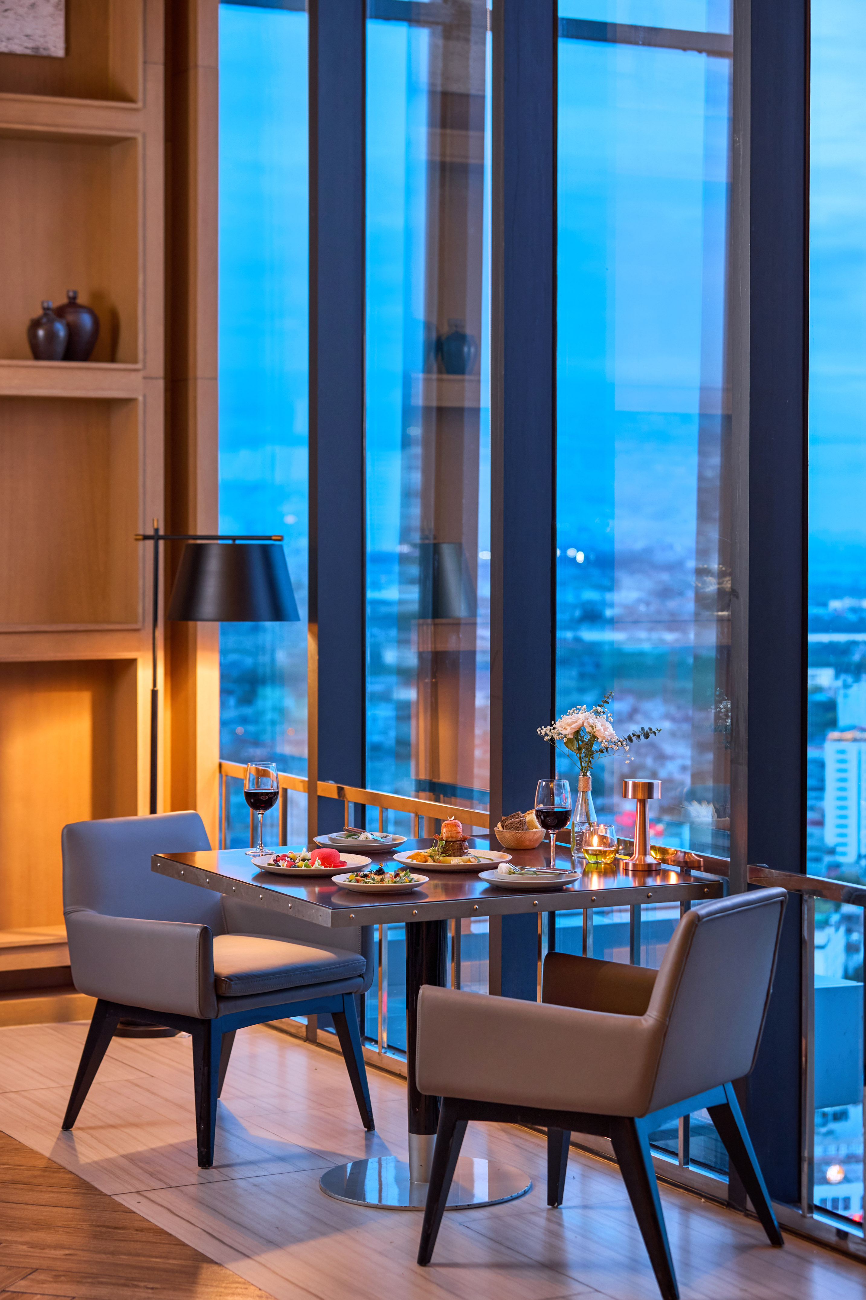 Elegant dinner table for two with food, wine, and evening city views.