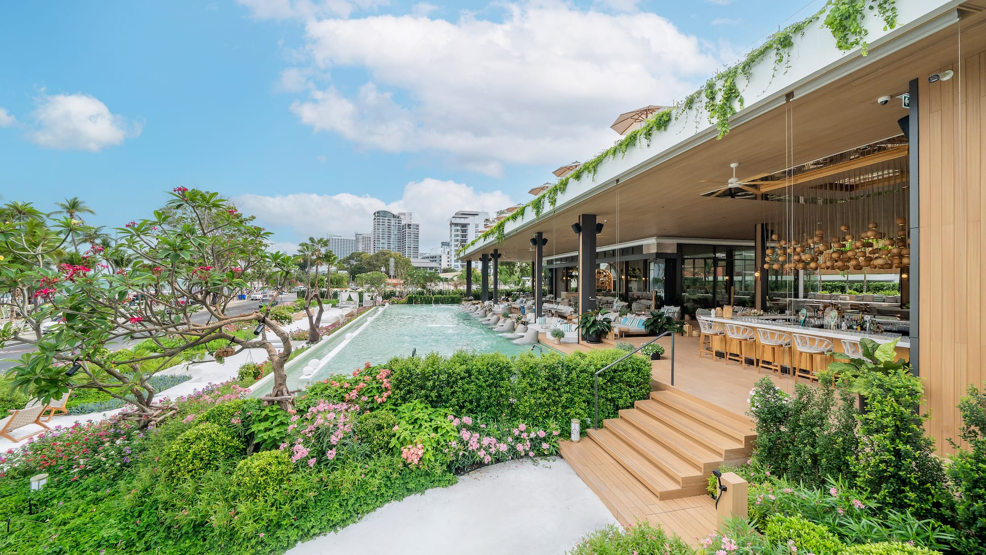 Luxury outdoor resort patio bar with pool, tropical garden, and city view.