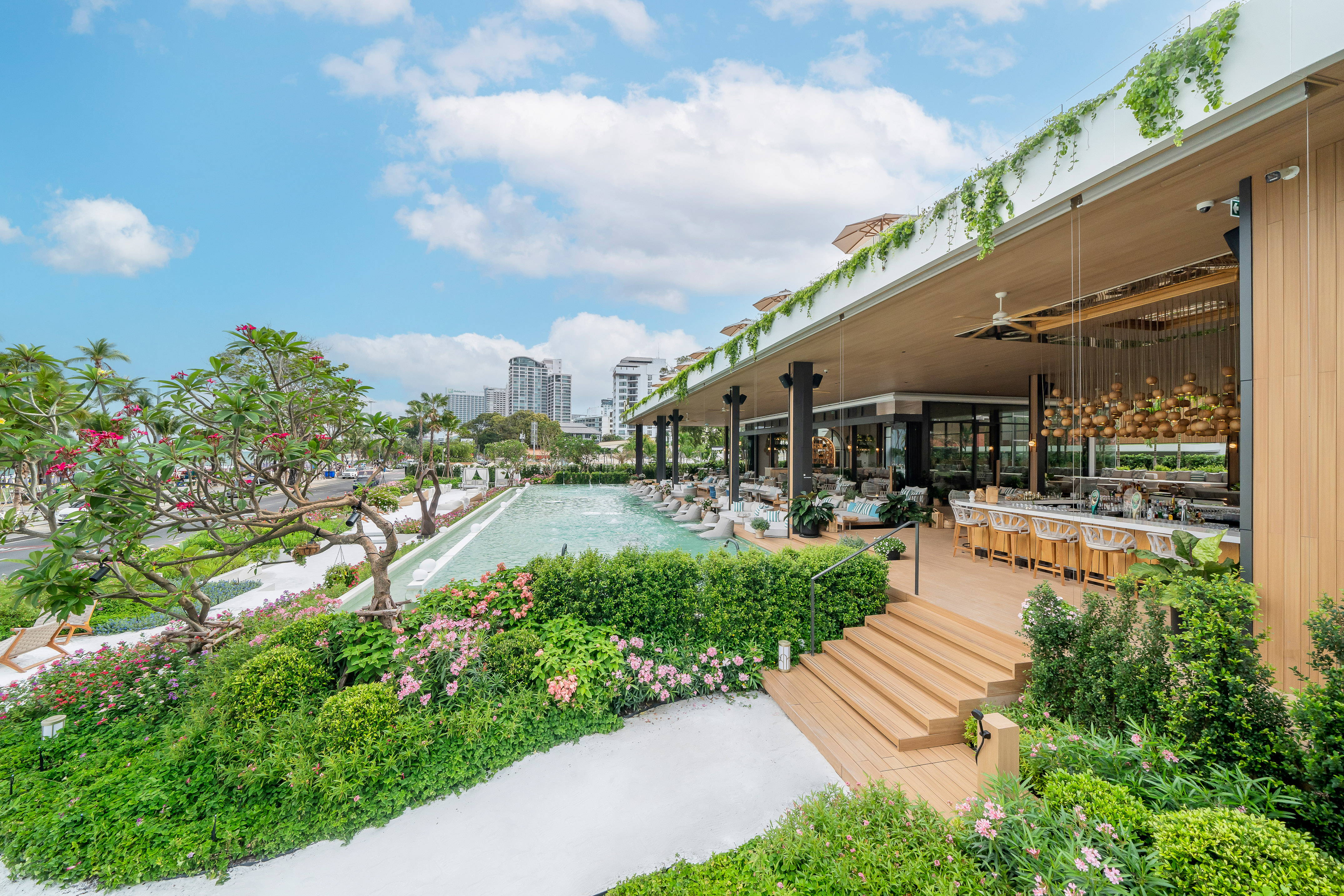 Luxury outdoor resort patio bar with pool, tropical garden, and city view.