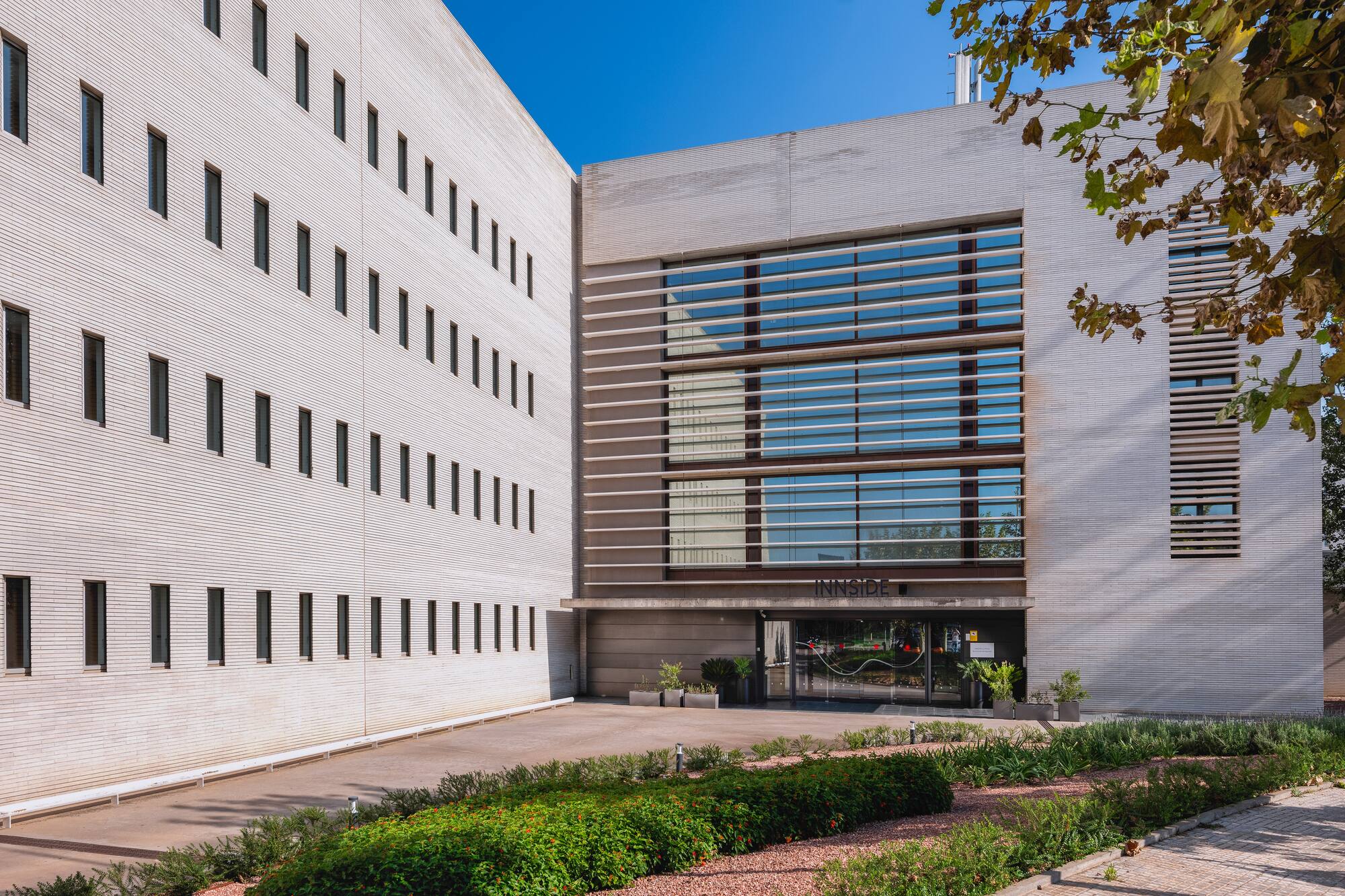 Innside hotel: modern white building, large glass entrance, green landscaping.
