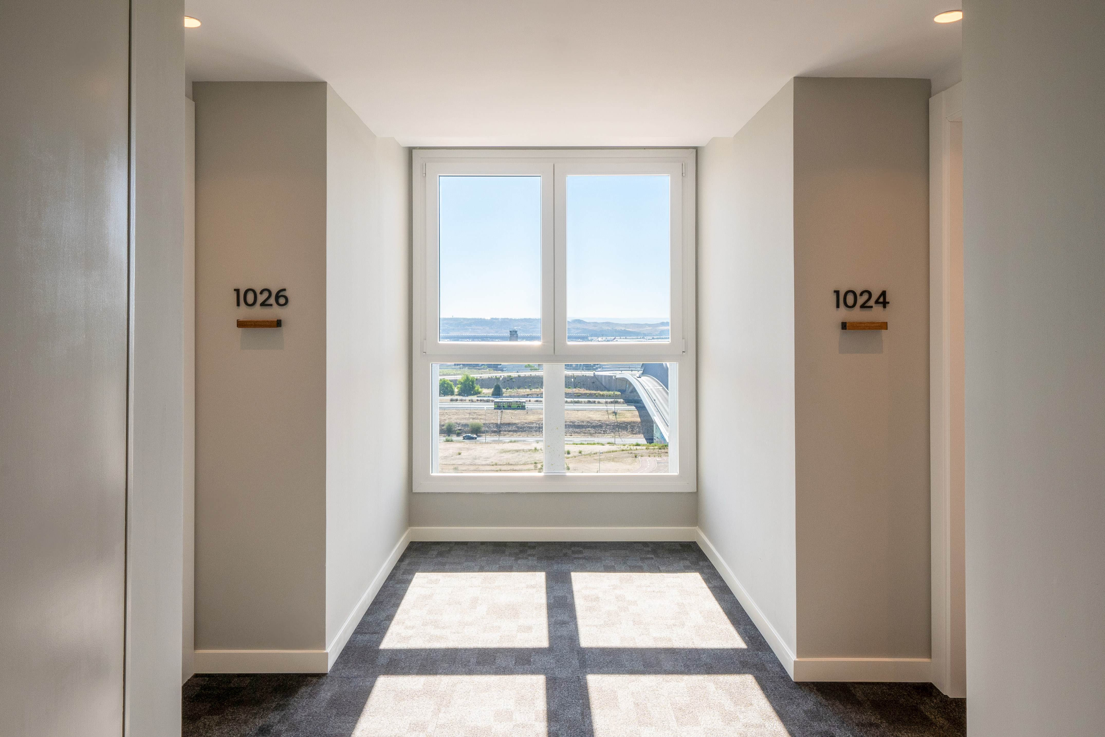 Bright modern hotel corridor with window view, room numbers 1024 and 1026.