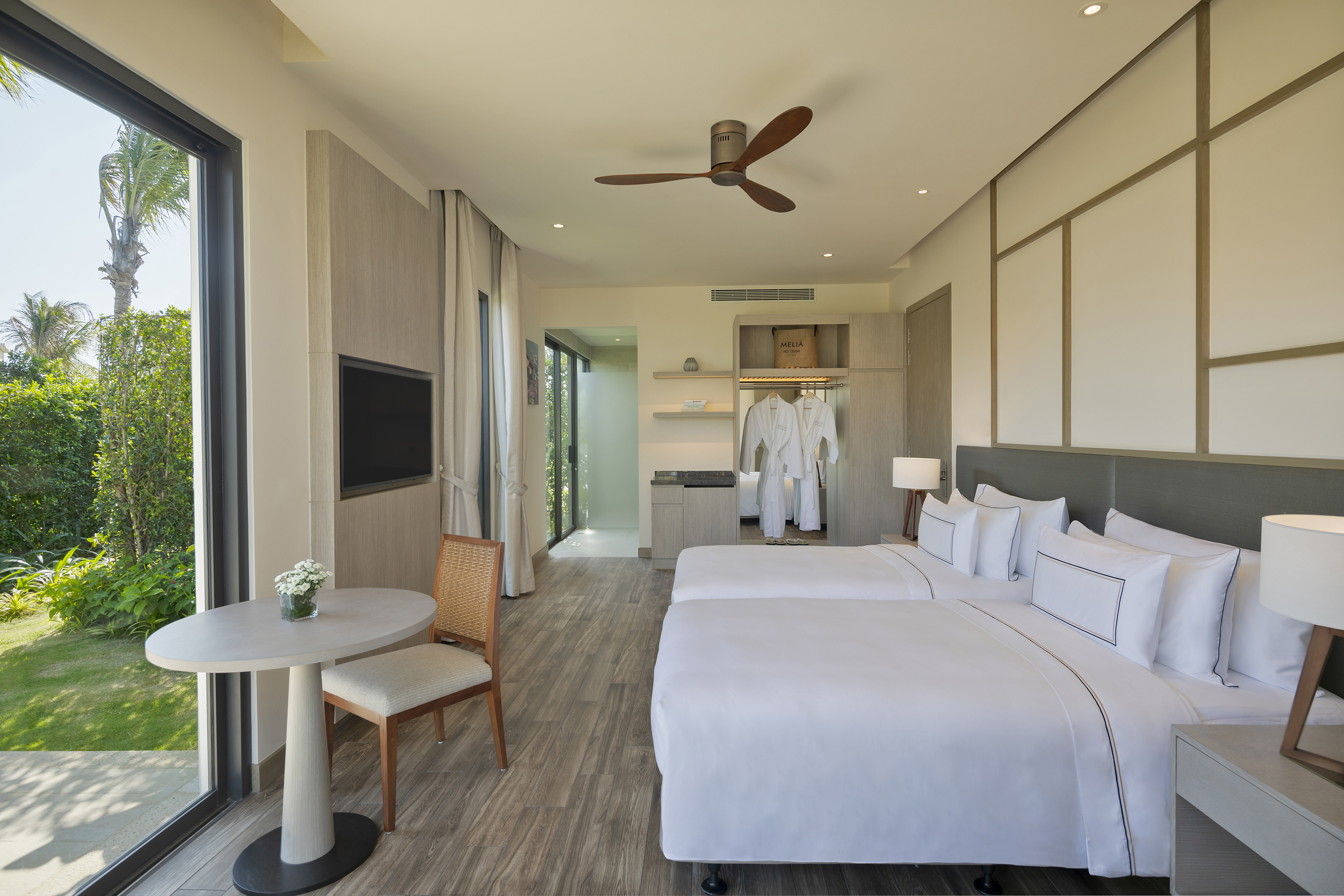 Modern hotel room with twin beds, lush garden view, and ceiling fan.