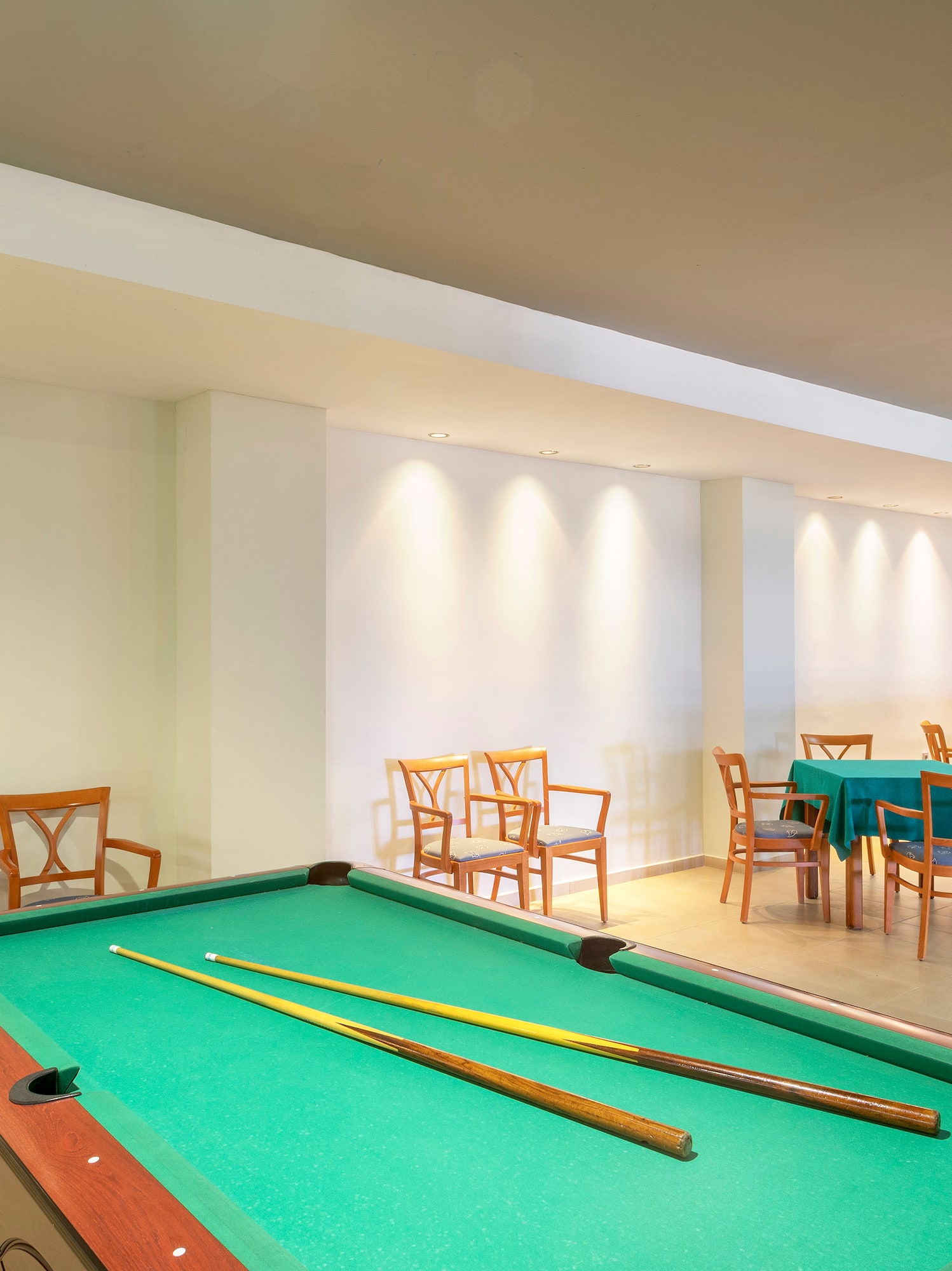 Hotel game room with a billiard table, cues, and small dining tables.