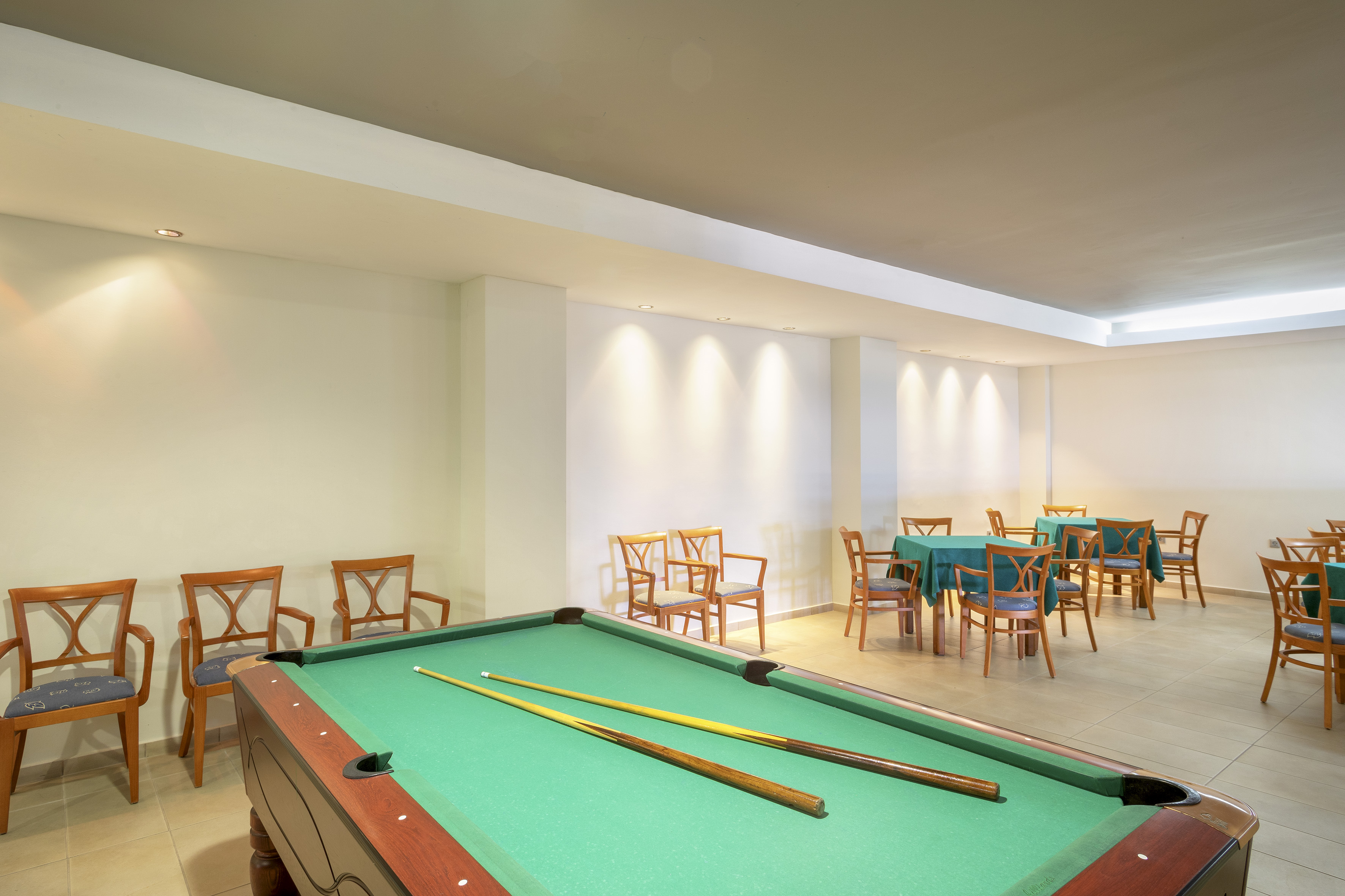 Hotel game room with a billiard table, cues, and small dining tables.