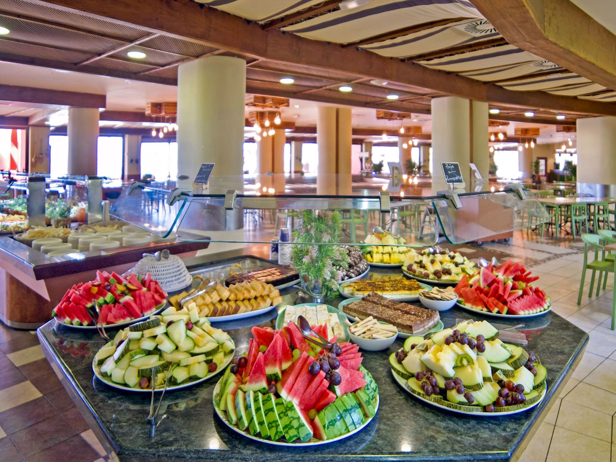 Buffet con frutas tropicales, pasteles y ensaladas en comedor de hotel.