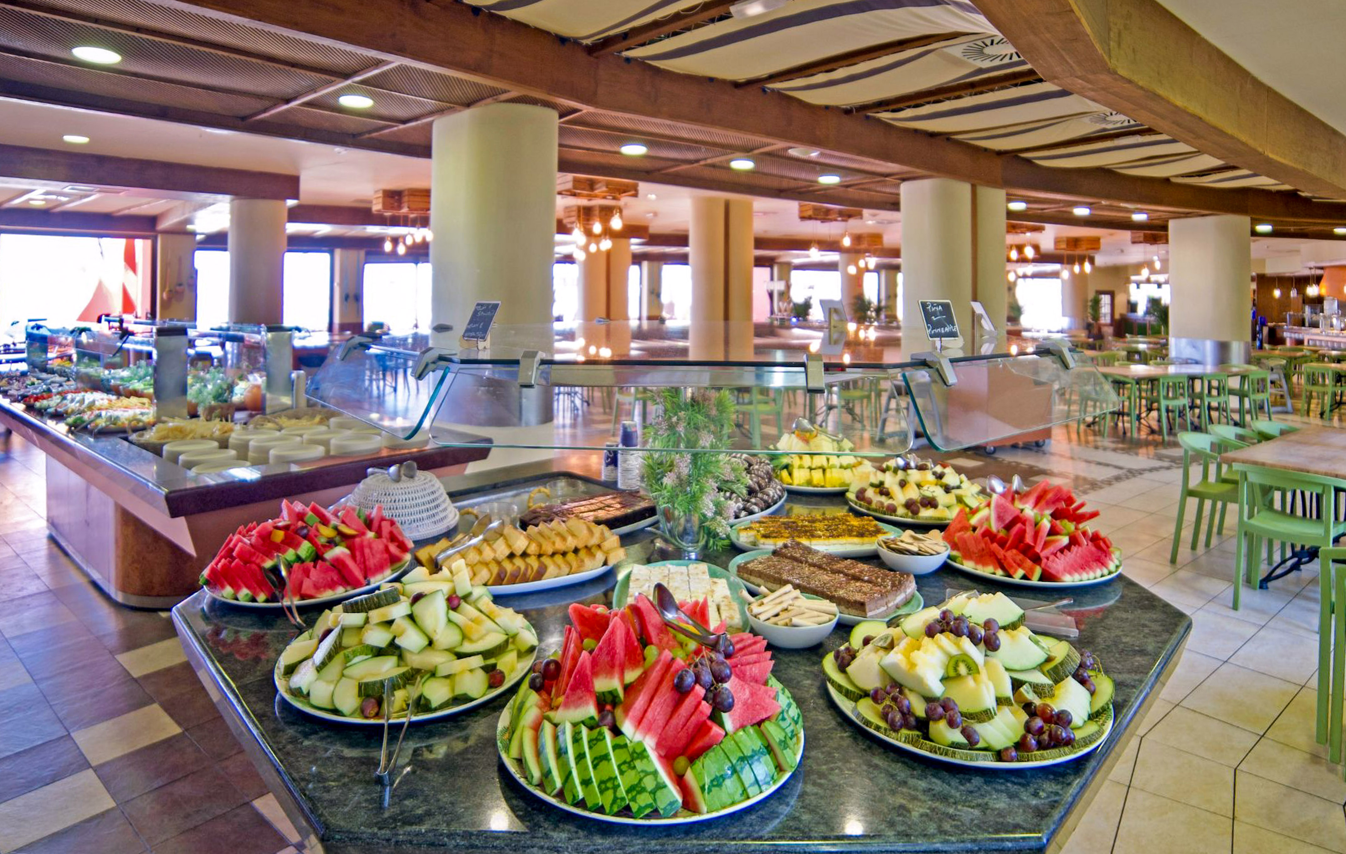 Buffet con frutas tropicales, pasteles y ensaladas en comedor de hotel.