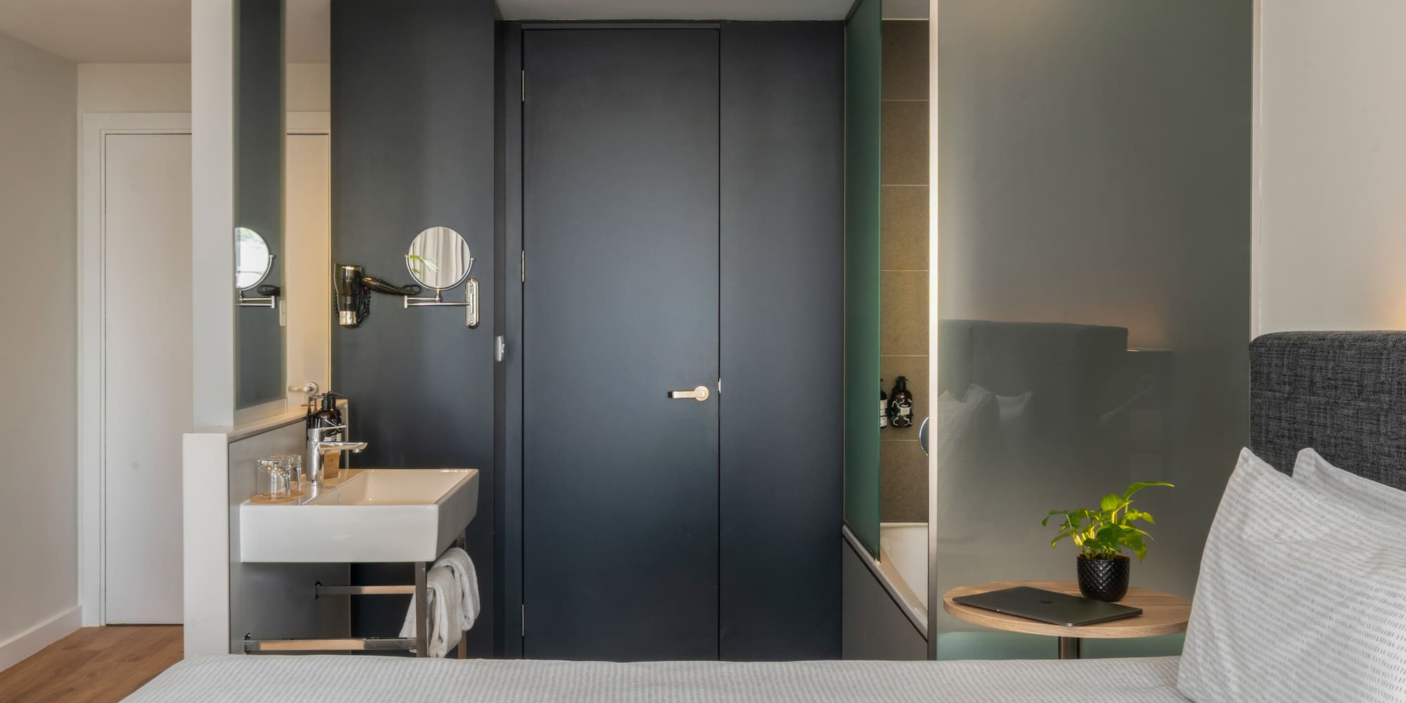 Modern hotel room with integrated sink, bed, and frosted glass tub.