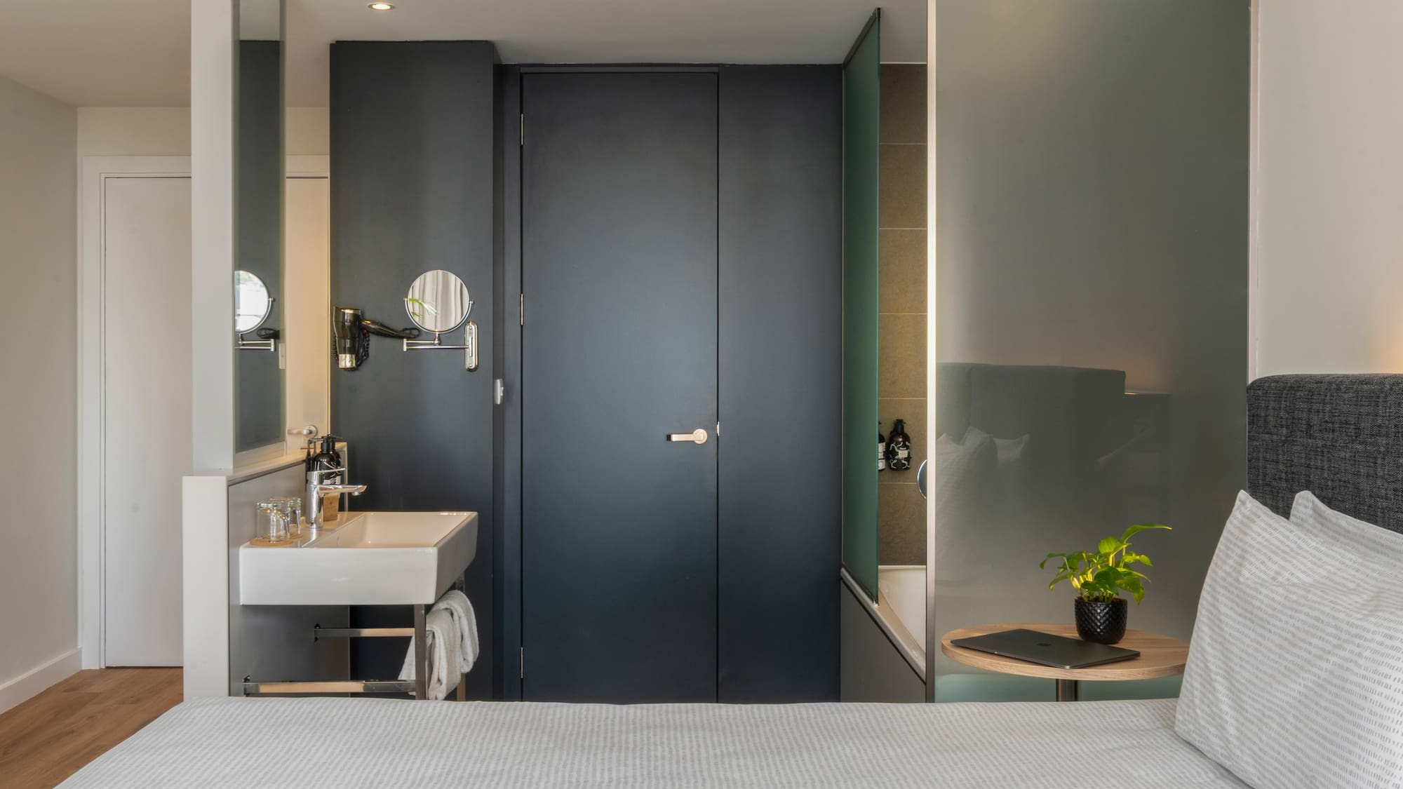 Modern hotel room with integrated sink, bed, and frosted glass tub.