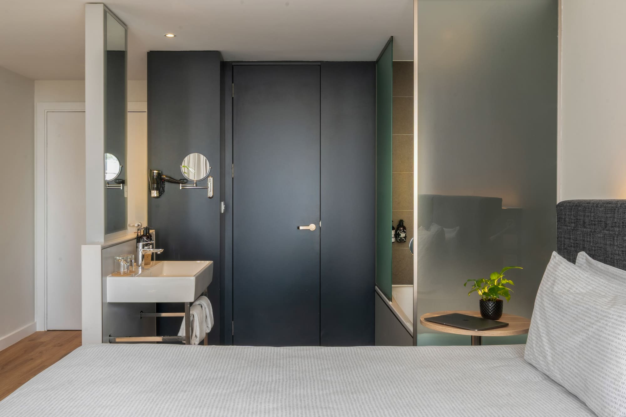 Modern hotel room with integrated sink, bed, and frosted glass tub.