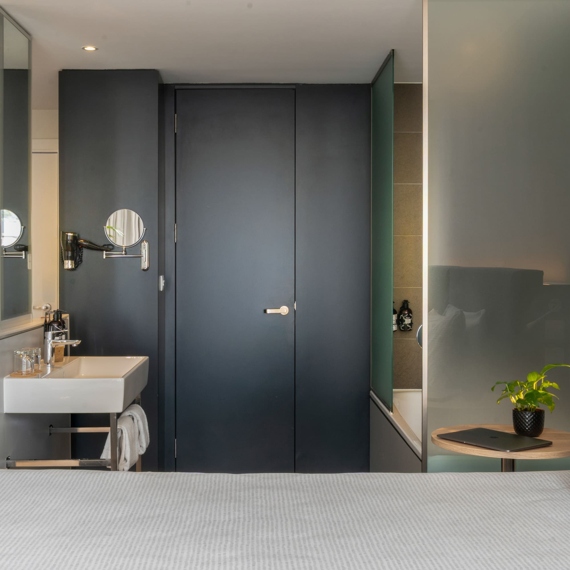 Modern hotel room with integrated sink, bed, and frosted glass tub.