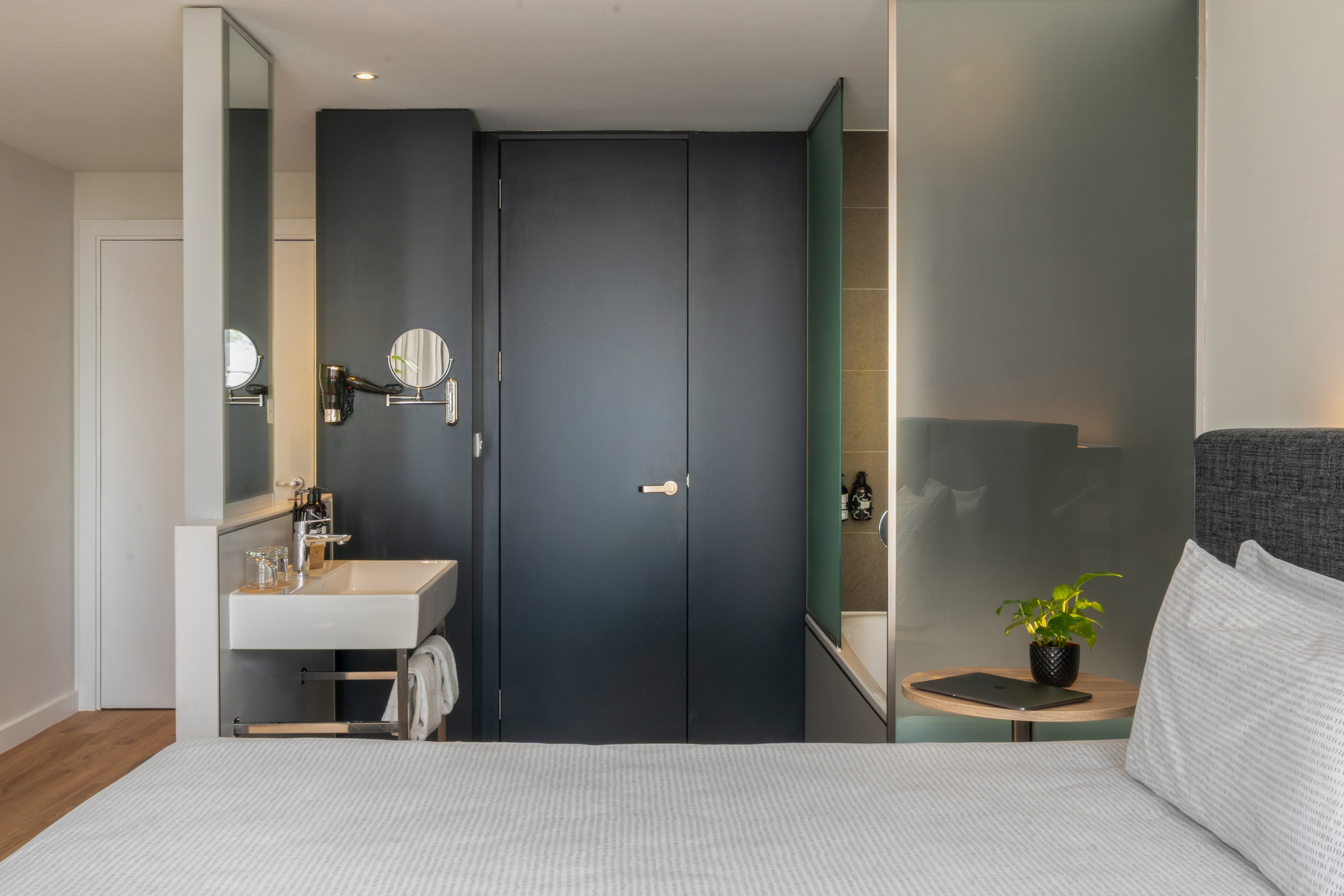 Modern hotel room with integrated sink, bed, and frosted glass tub.