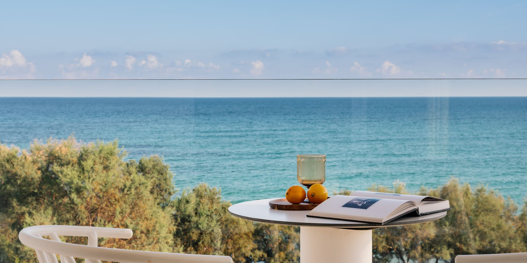 Relaxing ocean view balcony with book, glass, lemons on white table.