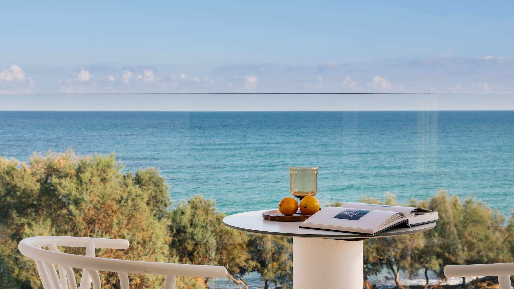 Relaxing ocean view balcony with book, glass, lemons on white table.