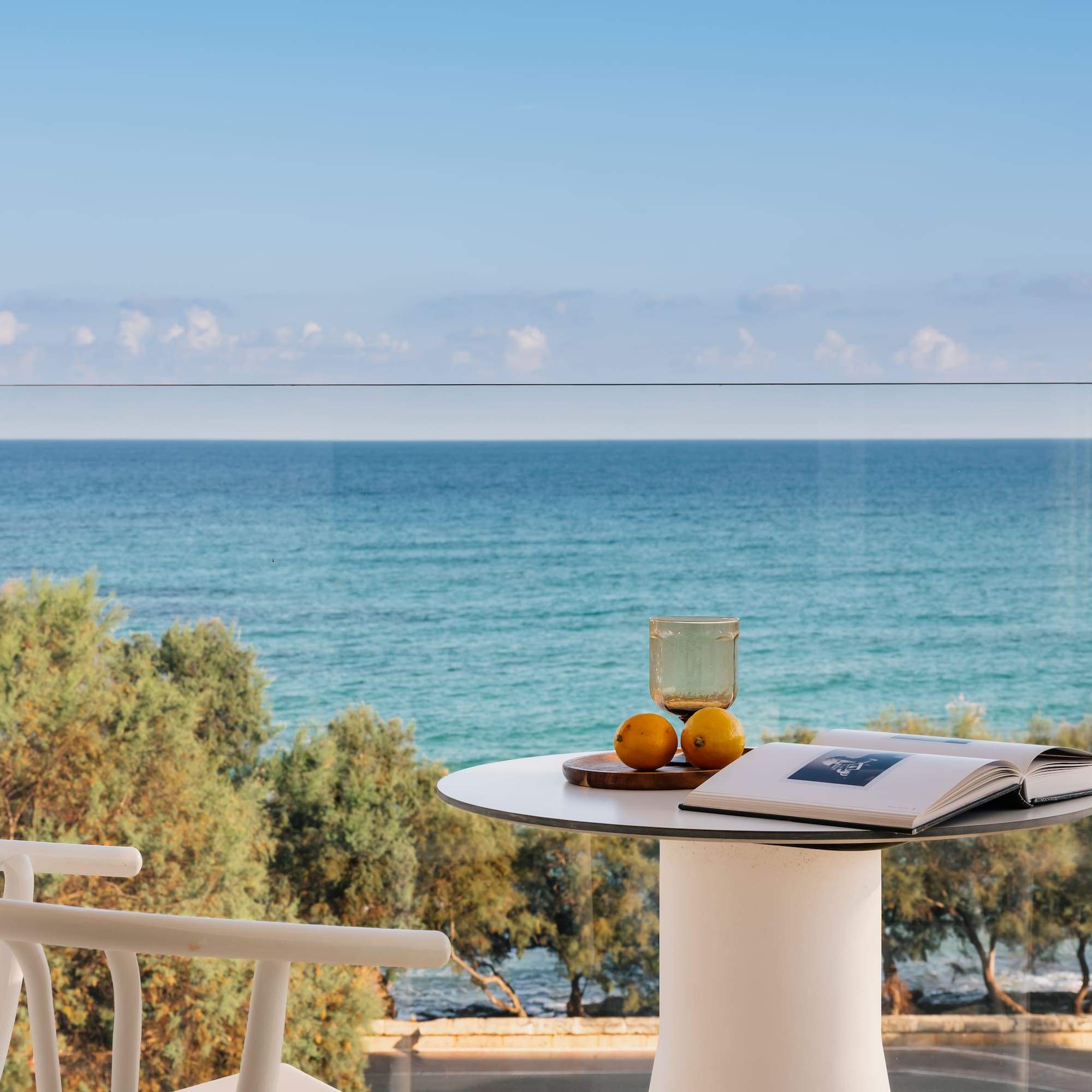 Relaxing ocean view balcony with book, glass, lemons on white table.