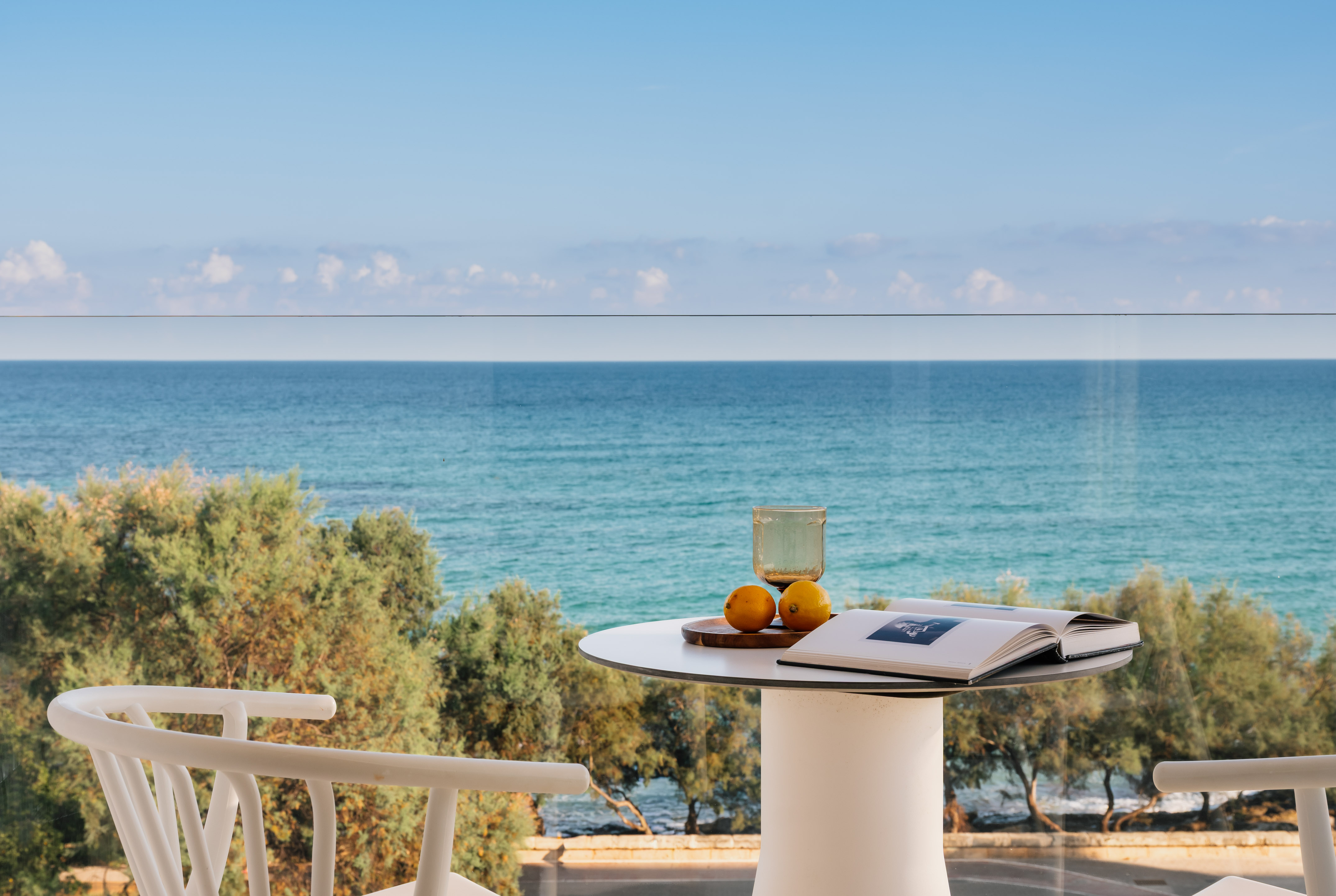 Relaxing ocean view balcony with book, glass, lemons on white table.