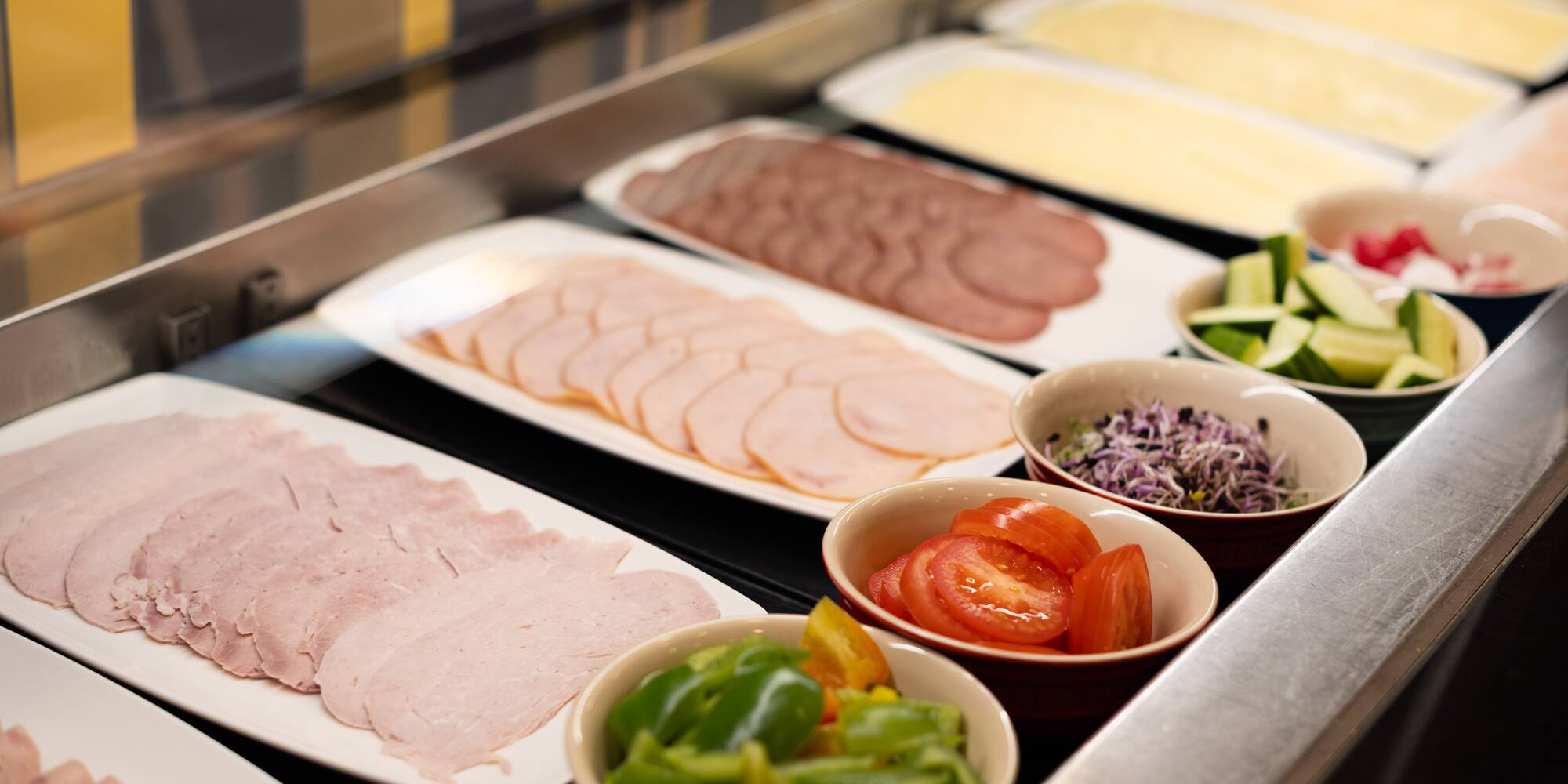Hotel breakfast buffet with sliced deli meats, cheese, and fresh vegetables.
