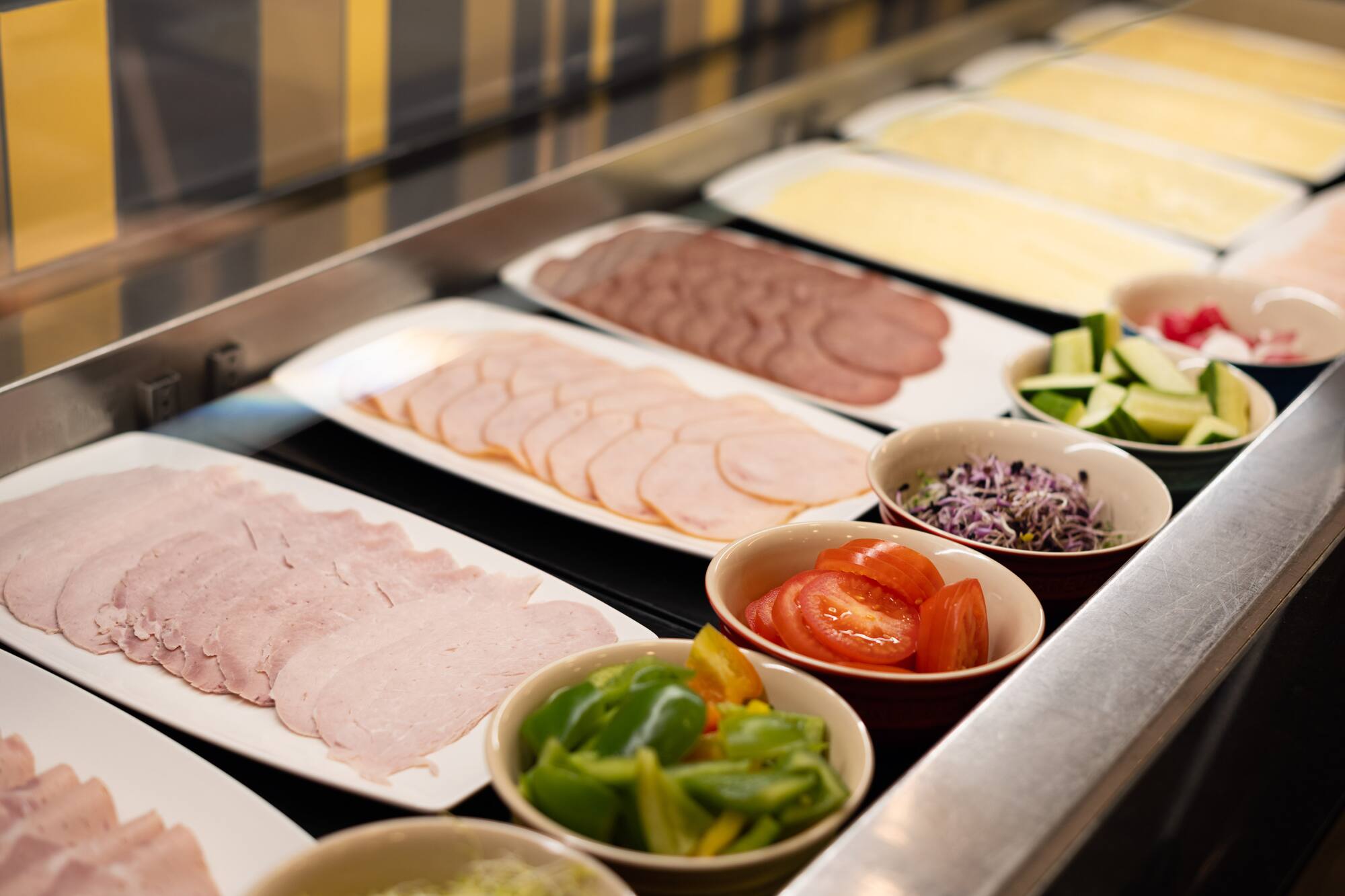 Breakfast deli buffet featuring cold cuts, cheeses, and fresh vegetables.