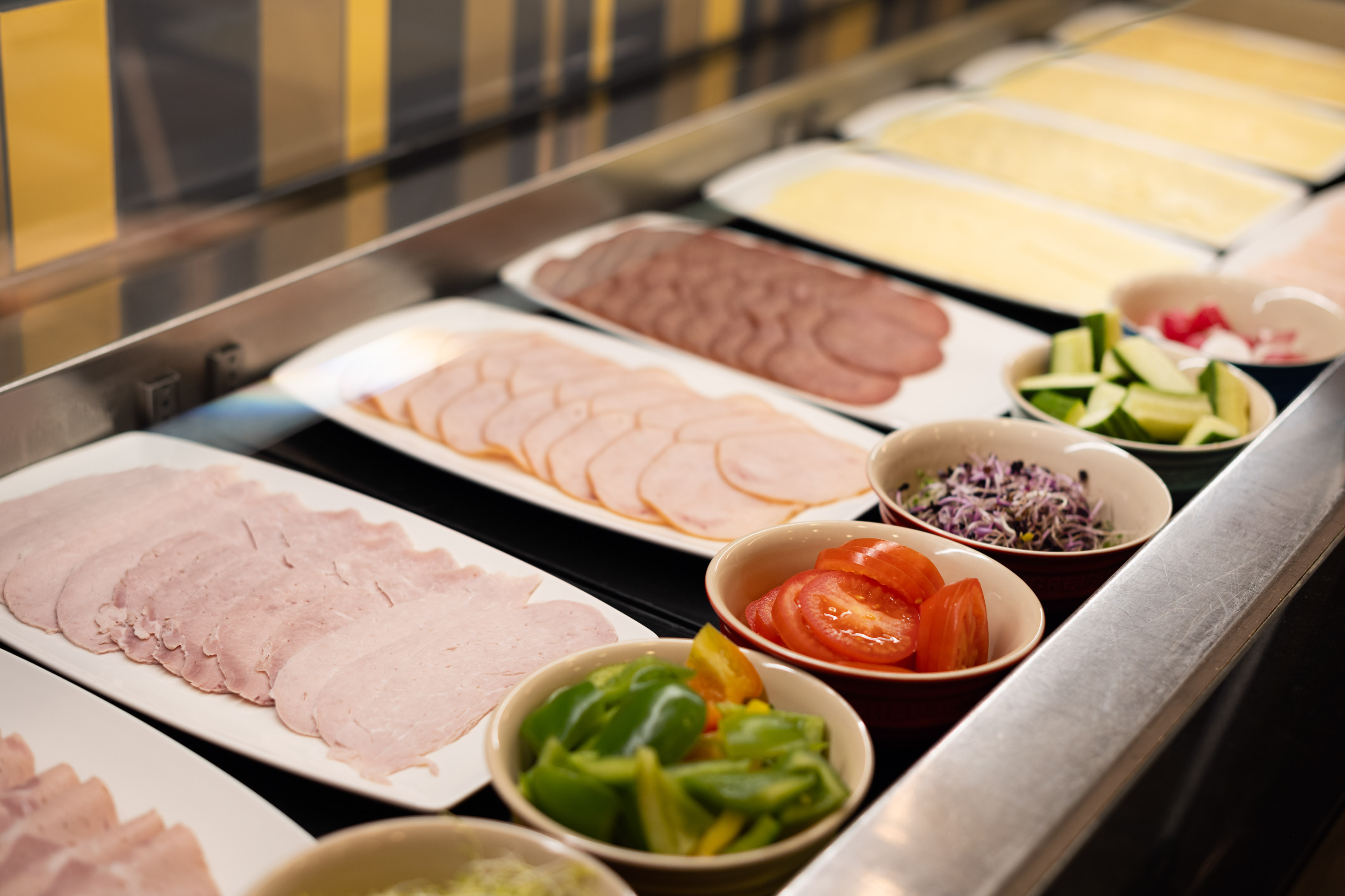 Hotel breakfast buffet with sliced deli meats, cheese, and fresh vegetables.