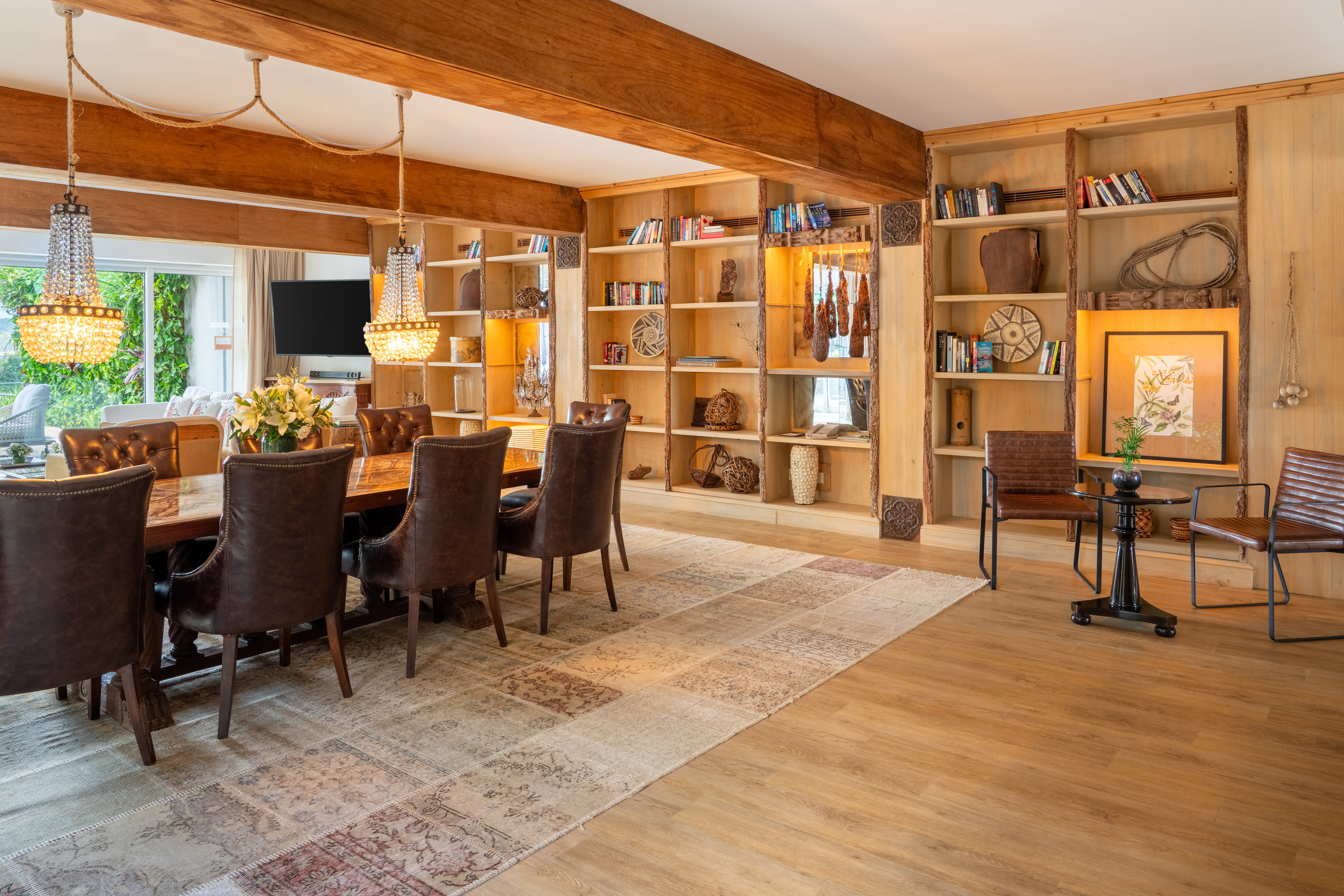 Elegant dining room with wooden table, leather chairs, chandeliers, and bookshelves.