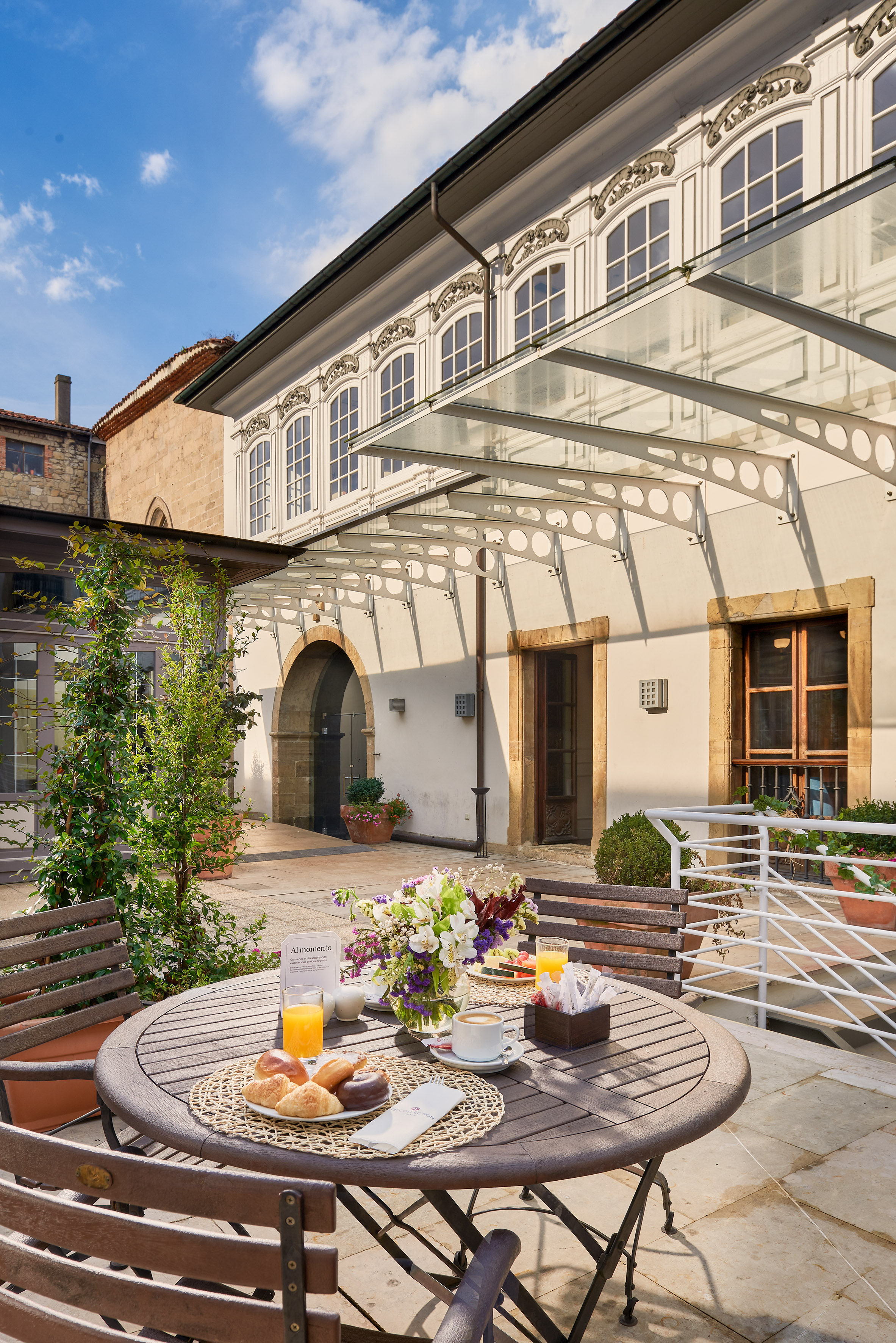 Courtyard breakfast with pastries, juice, coffee, and flowers, outside historic building. - Buffet Espolita, Cuisine internationale - Palacio de Avilés Affiliated by Meliá, Avilés
