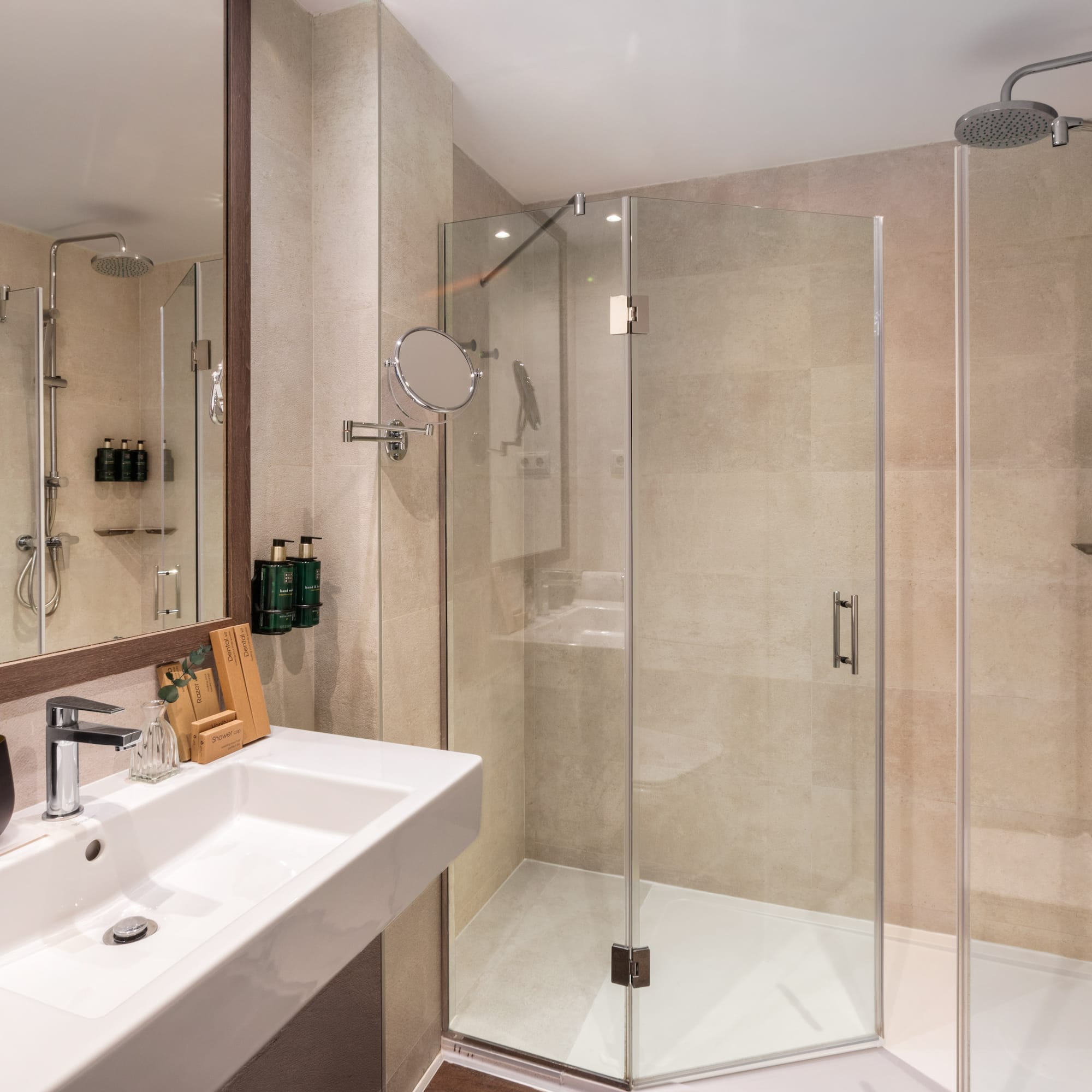 Modern hotel bathroom featuring white sink, mirror, and glass corner shower.