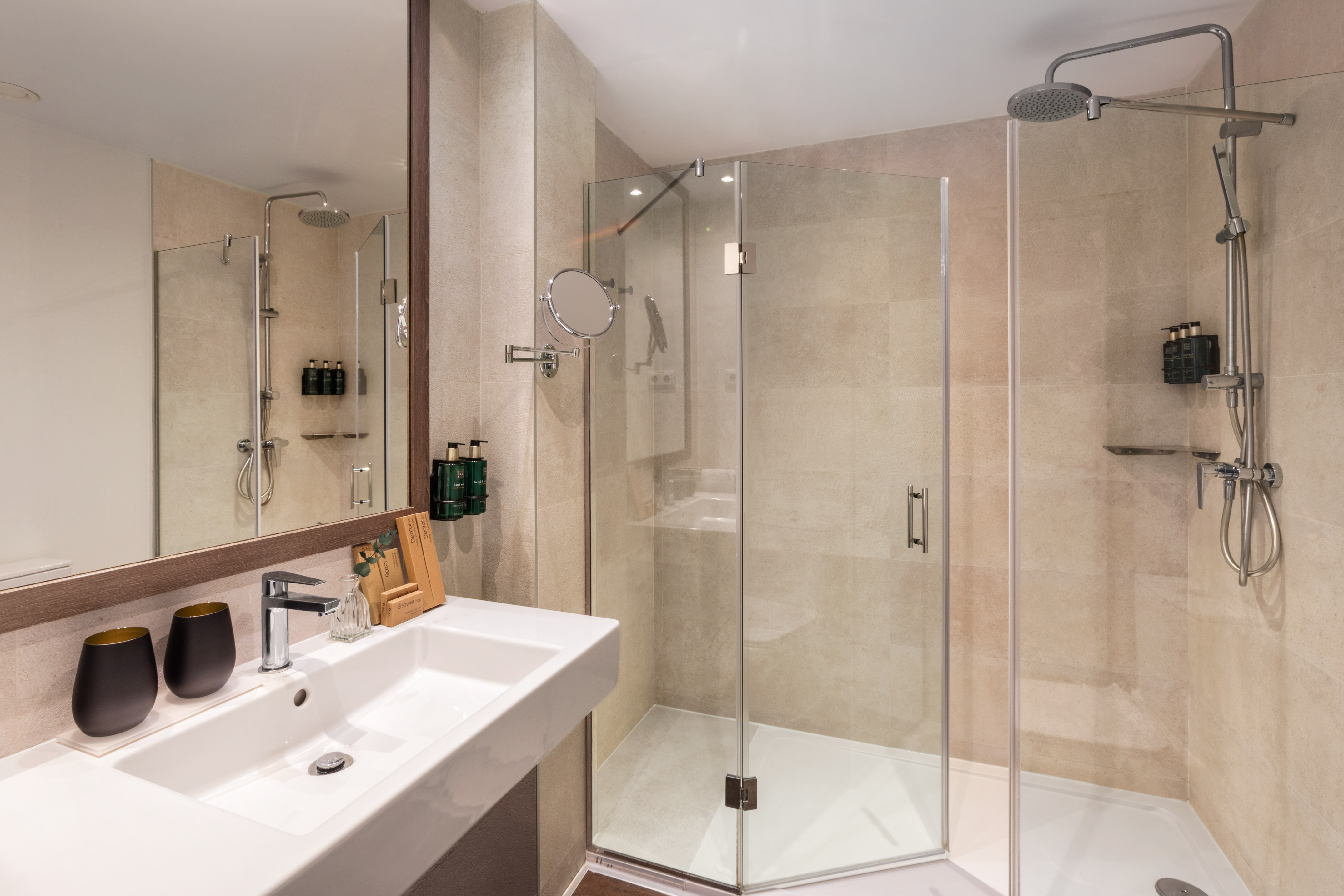 Modern hotel bathroom featuring white sink, mirror, and glass corner shower.
