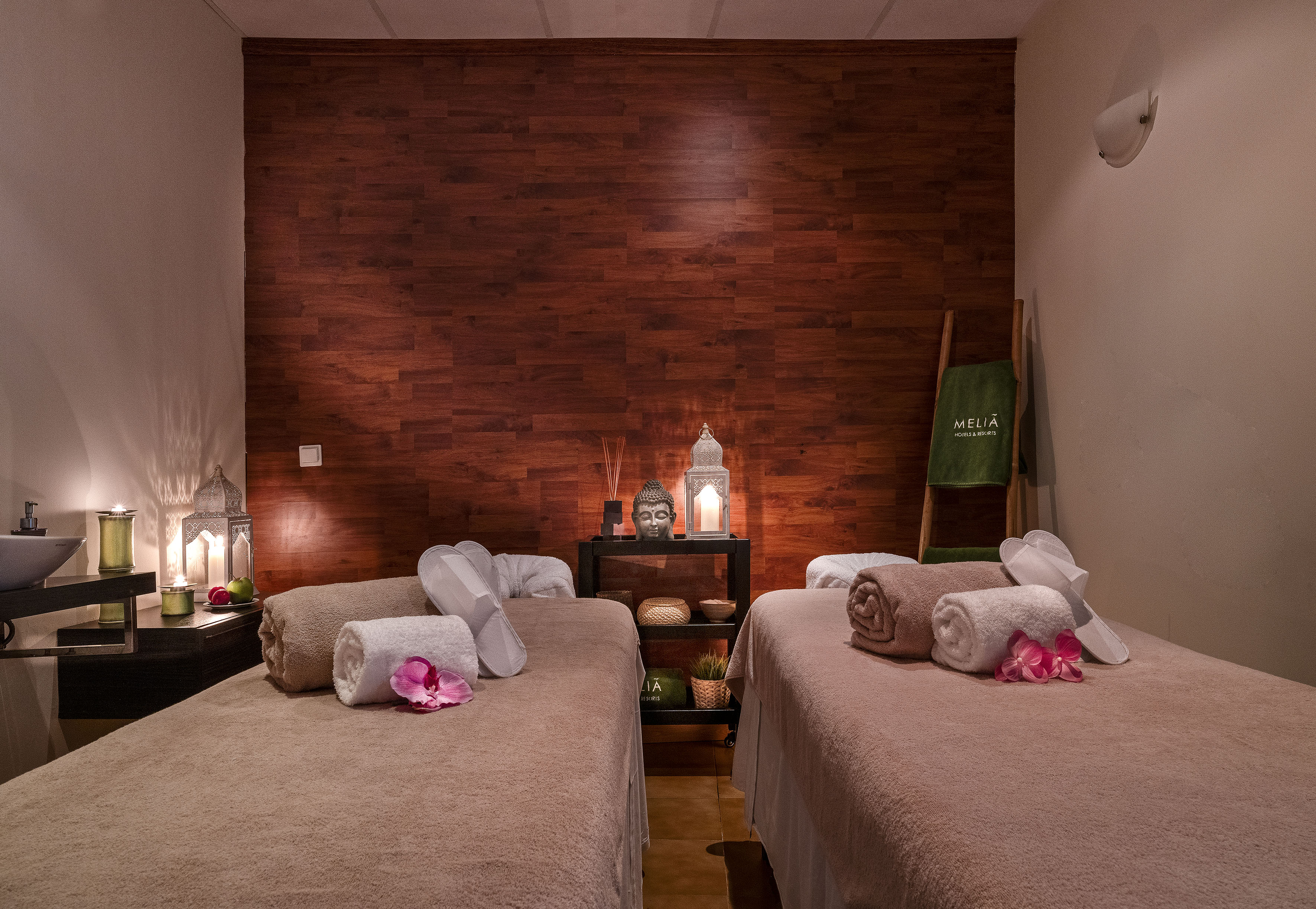 Meliá spa room with two massage beds, lanterns, Buddha, and towels.