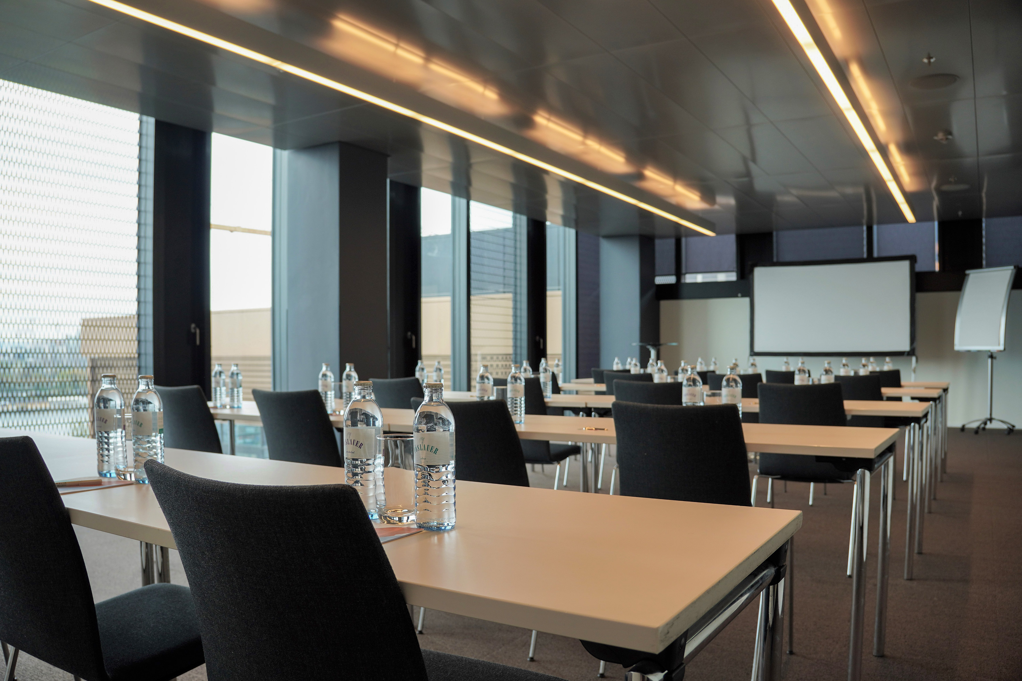 Modern meeting room set up with tables, chairs, water bottles, projector.