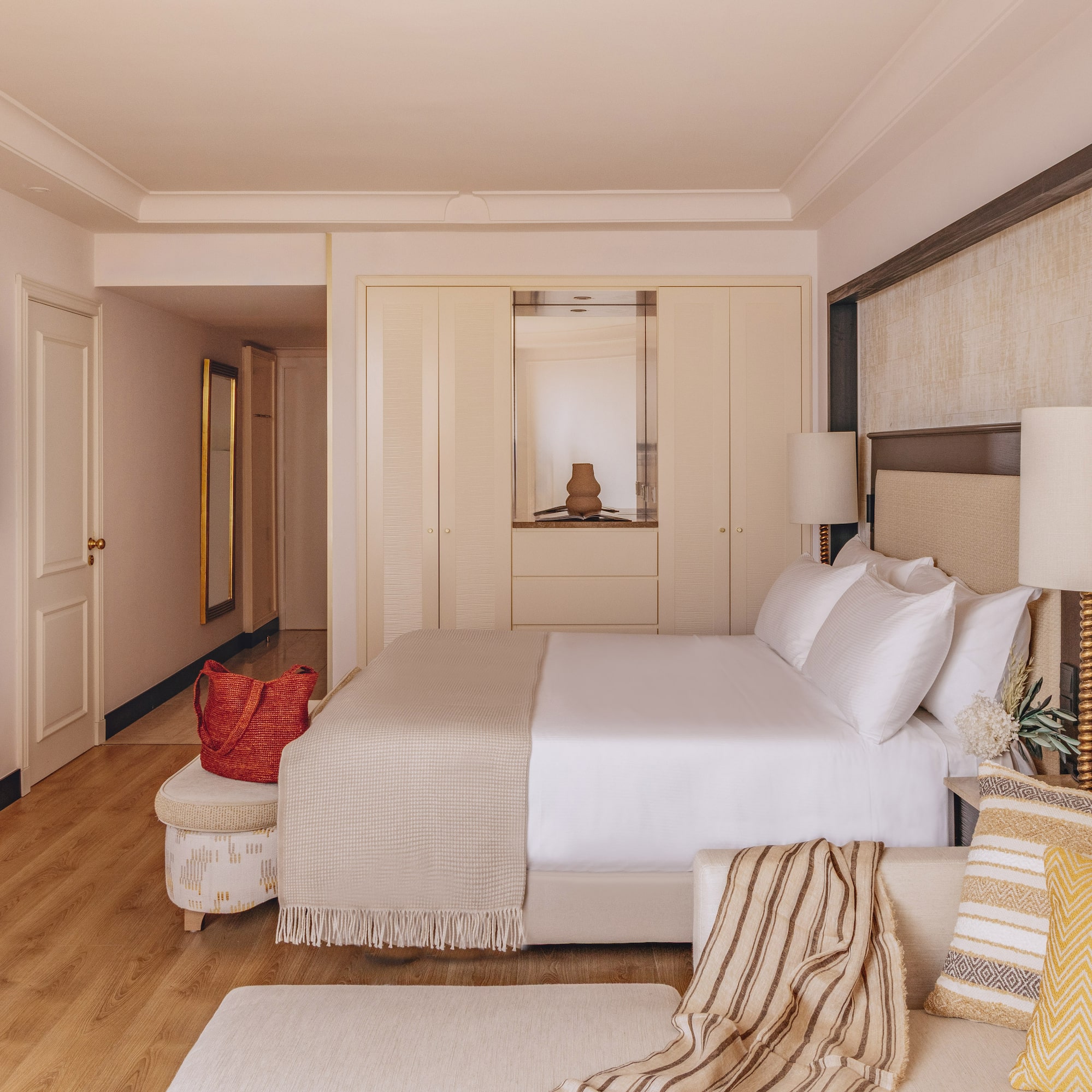 Bright, modern hotel room with bed, sofa, TV, built-in wardrobe, and wood floor.