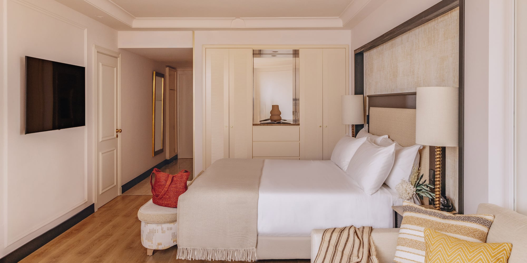 Bright, modern hotel room with bed, sofa, TV, built-in wardrobe, and wood floor.