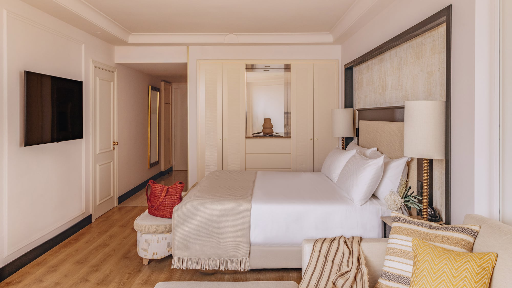 Bright, modern hotel room with bed, sofa, TV, built-in wardrobe, and wood floor.