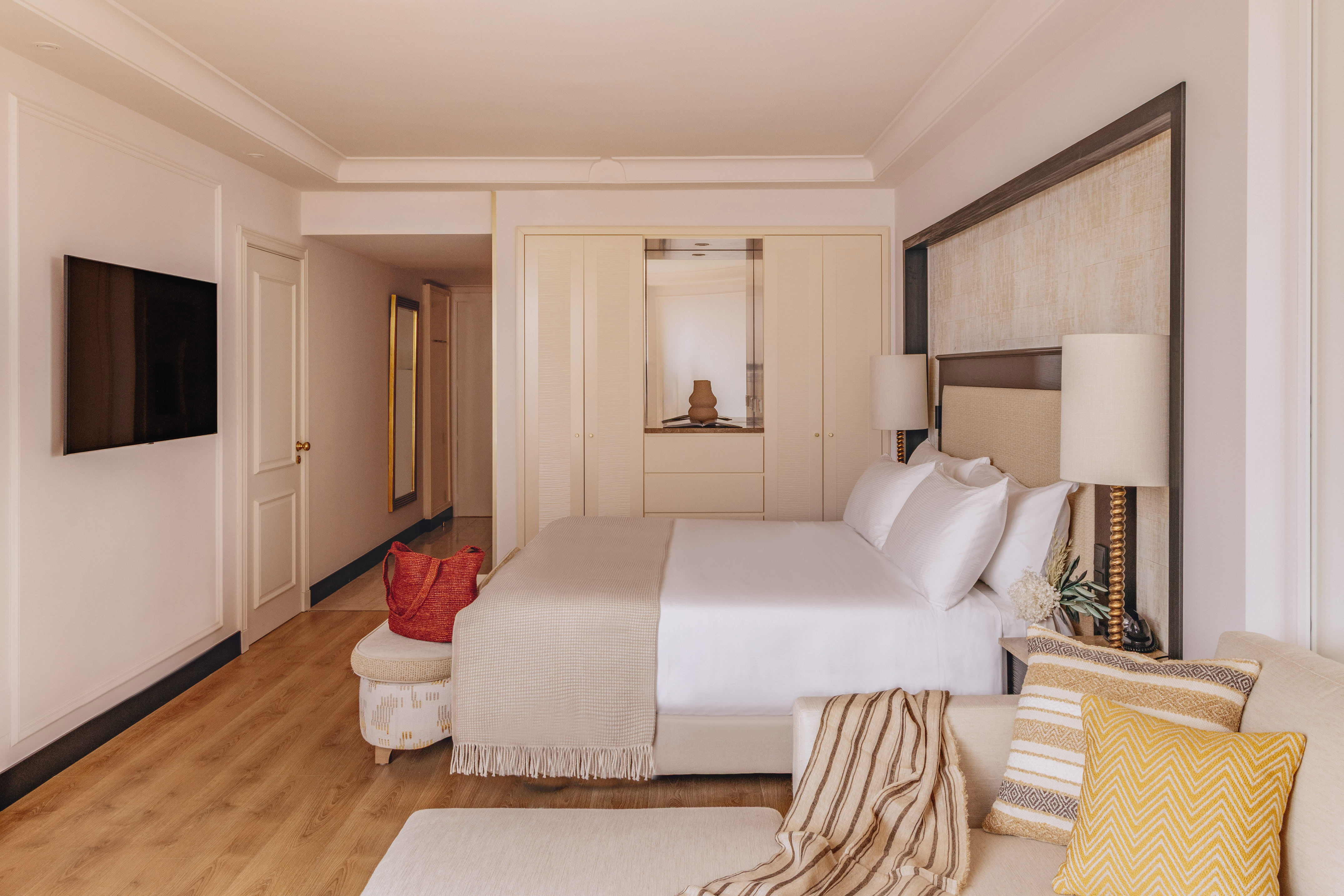 Bright, modern hotel room with bed, sofa, TV, built-in wardrobe, and wood floor.