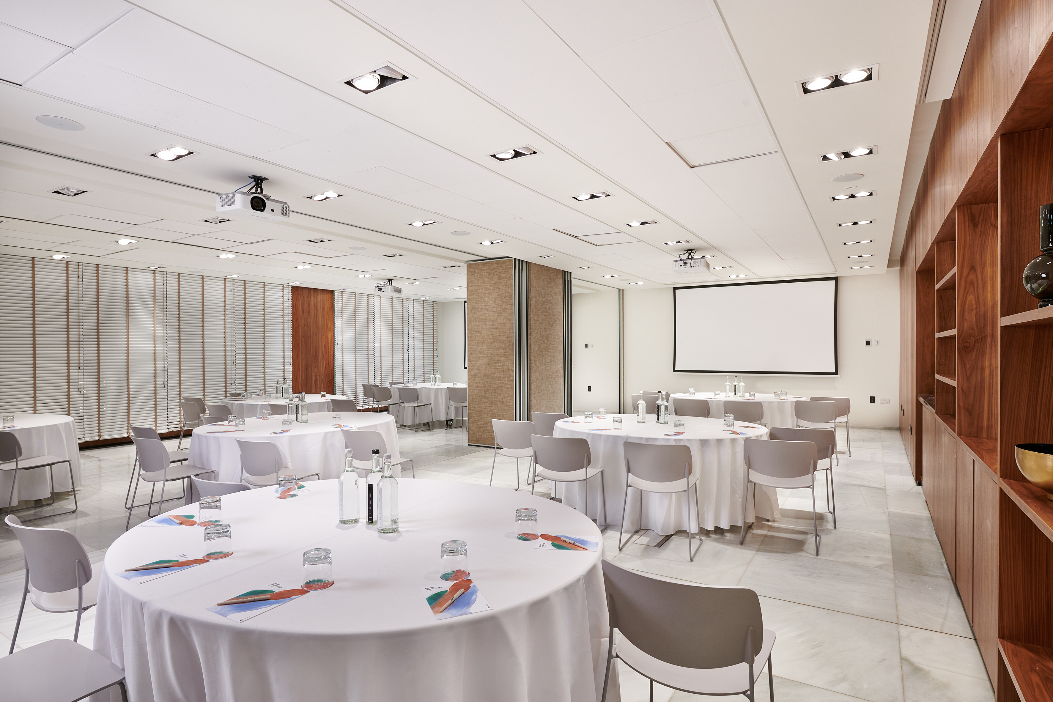 Modern conference room with round tables, projector screen, and partition walls.