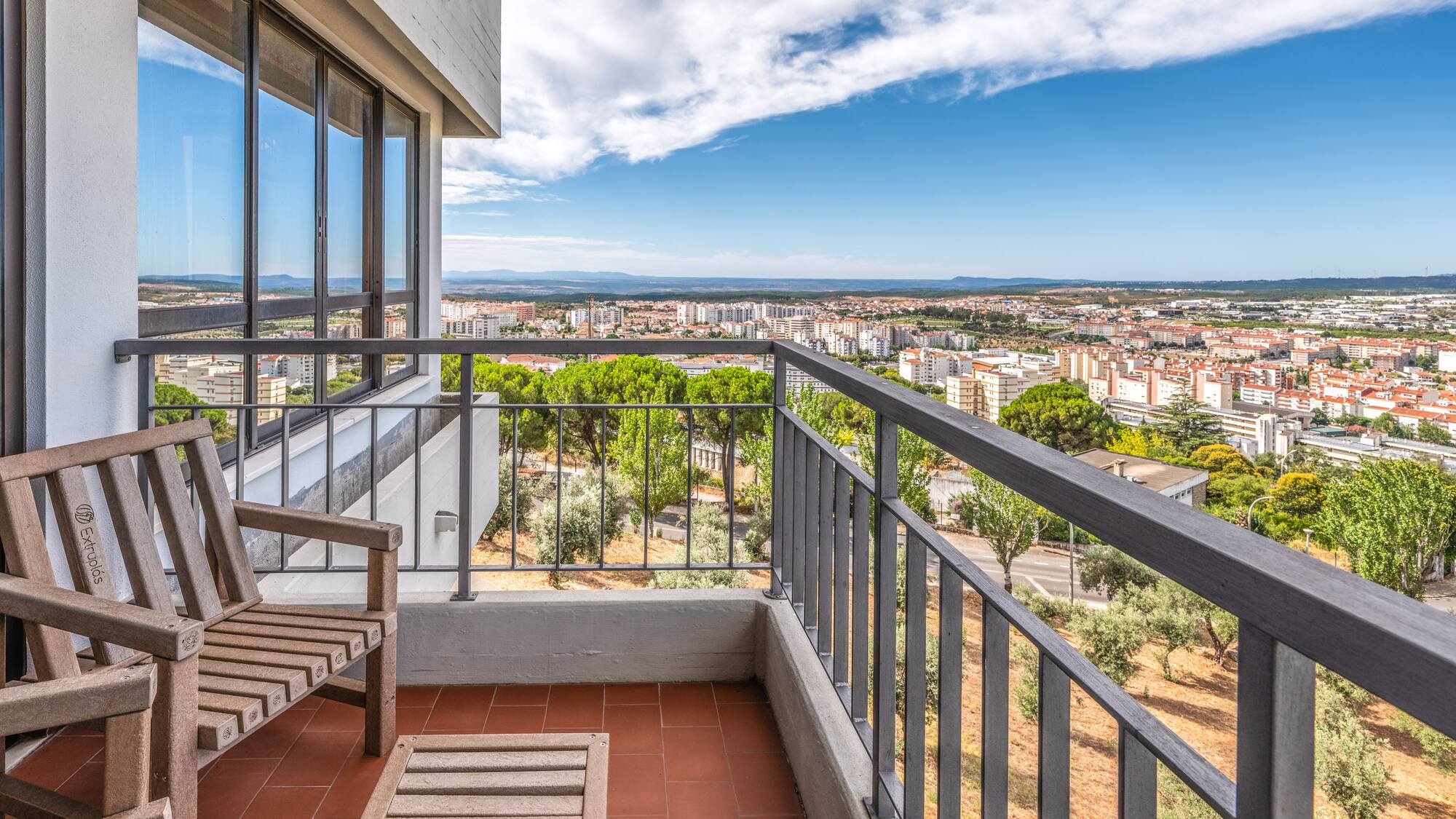 Balcony with wooden chairs, terracotta floor, and panoramic city views.