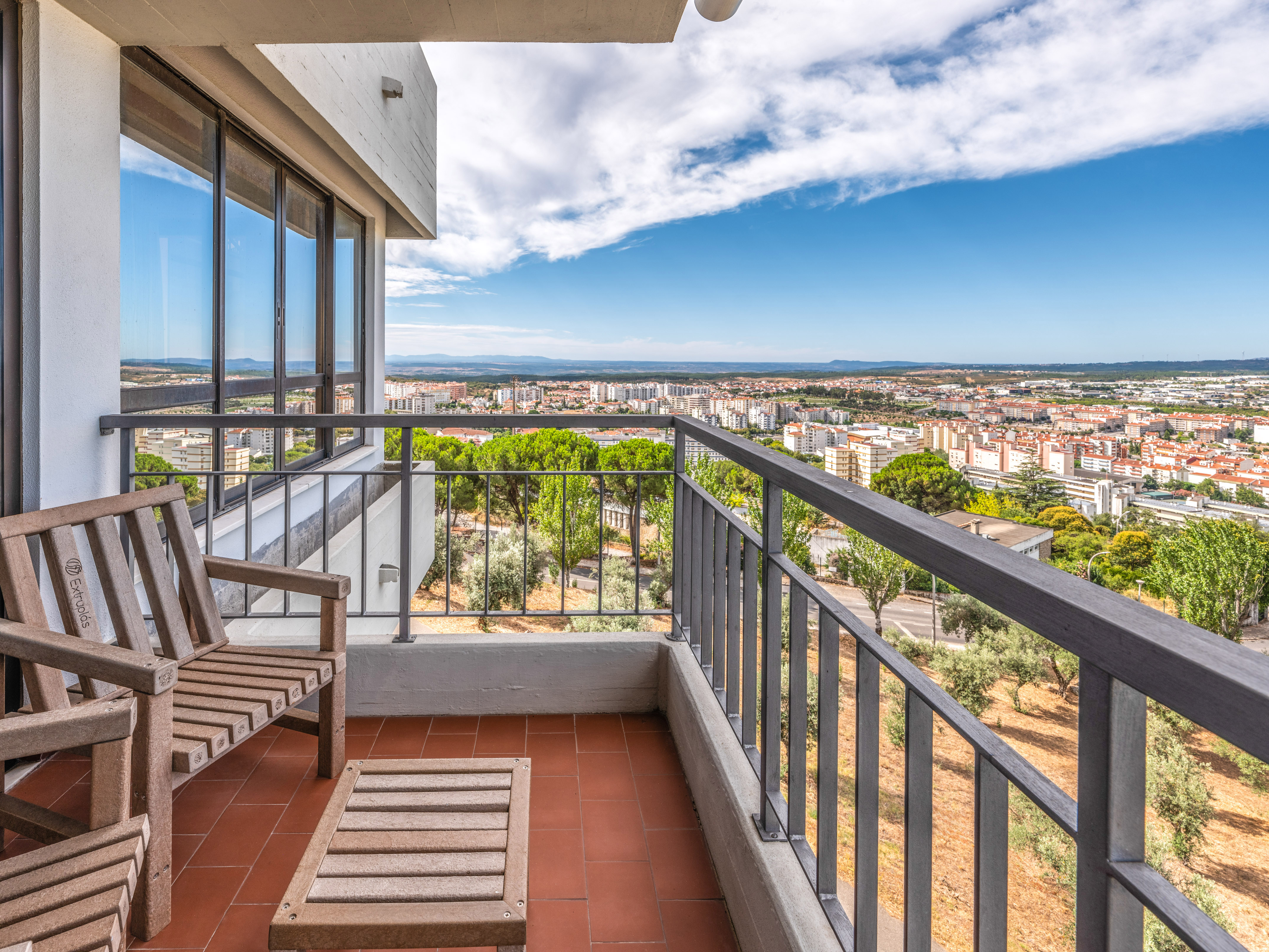 Balcony with wooden chairs, terracotta floor, and panoramic city views.