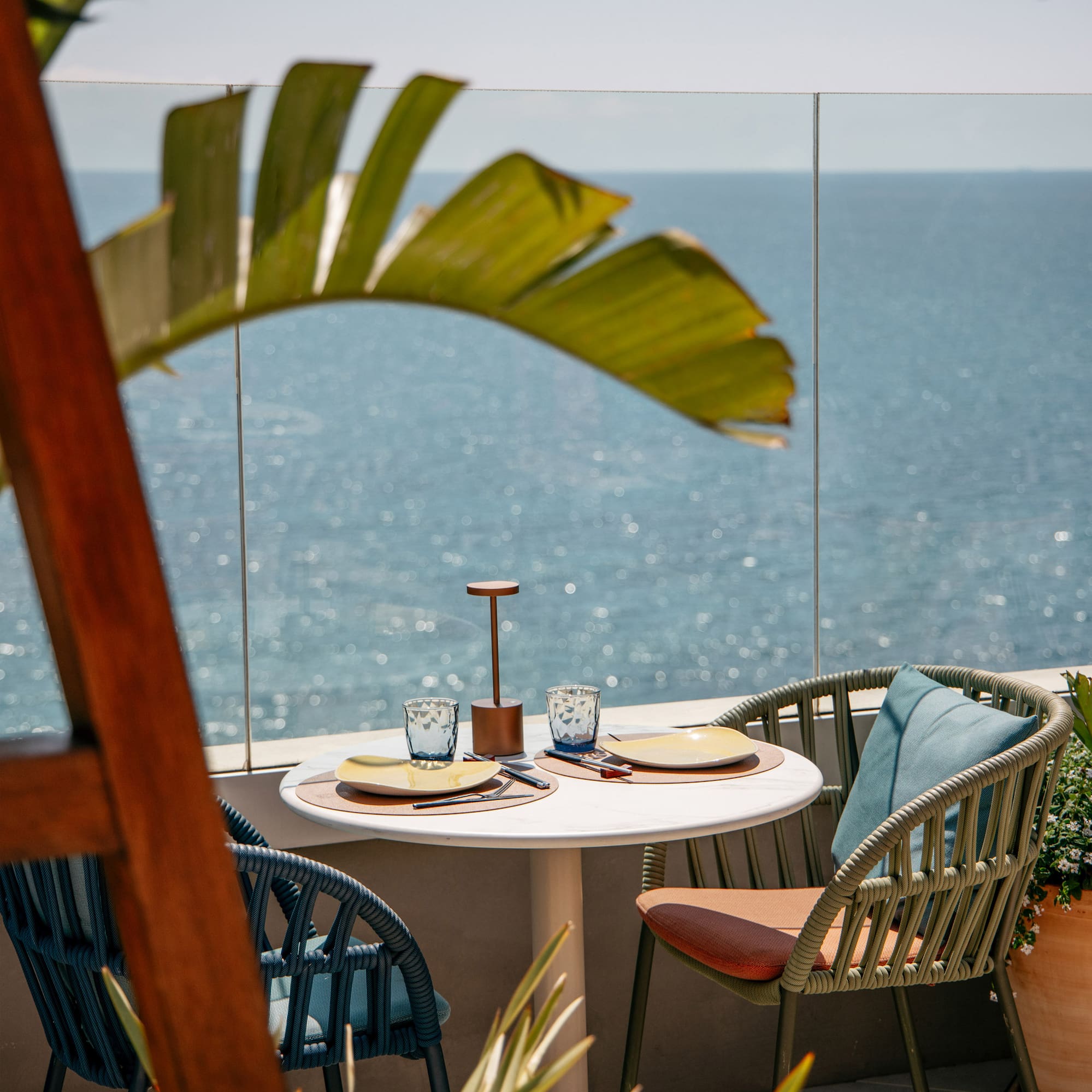 a table with chairs and a glass fence overlooking the ocean