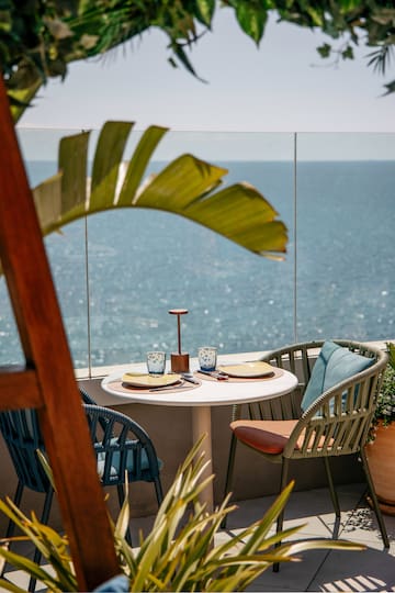 a table with chairs and a glass fence overlooking the ocean