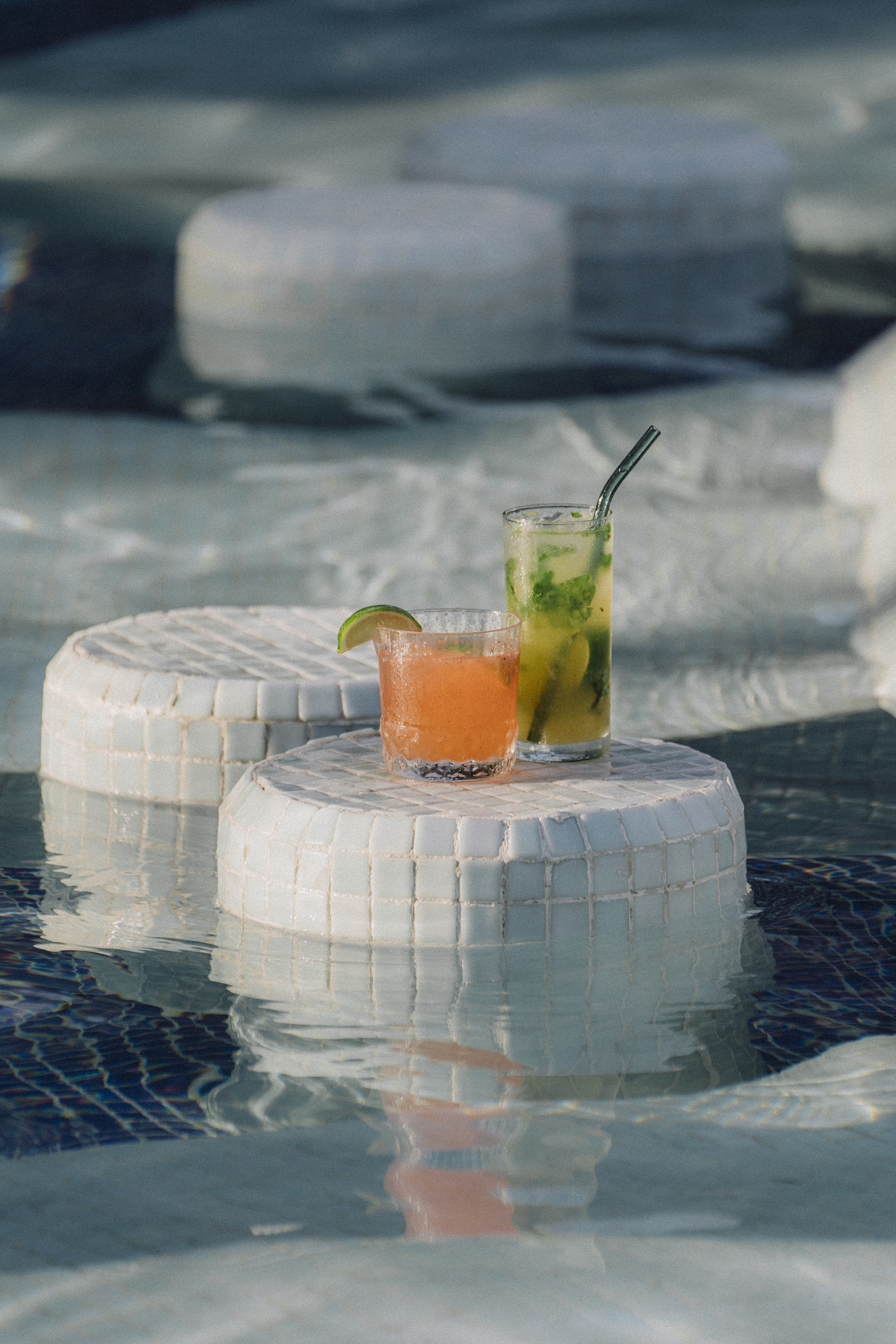 Orange and green cocktails on tiled tables in a swimming pool.
