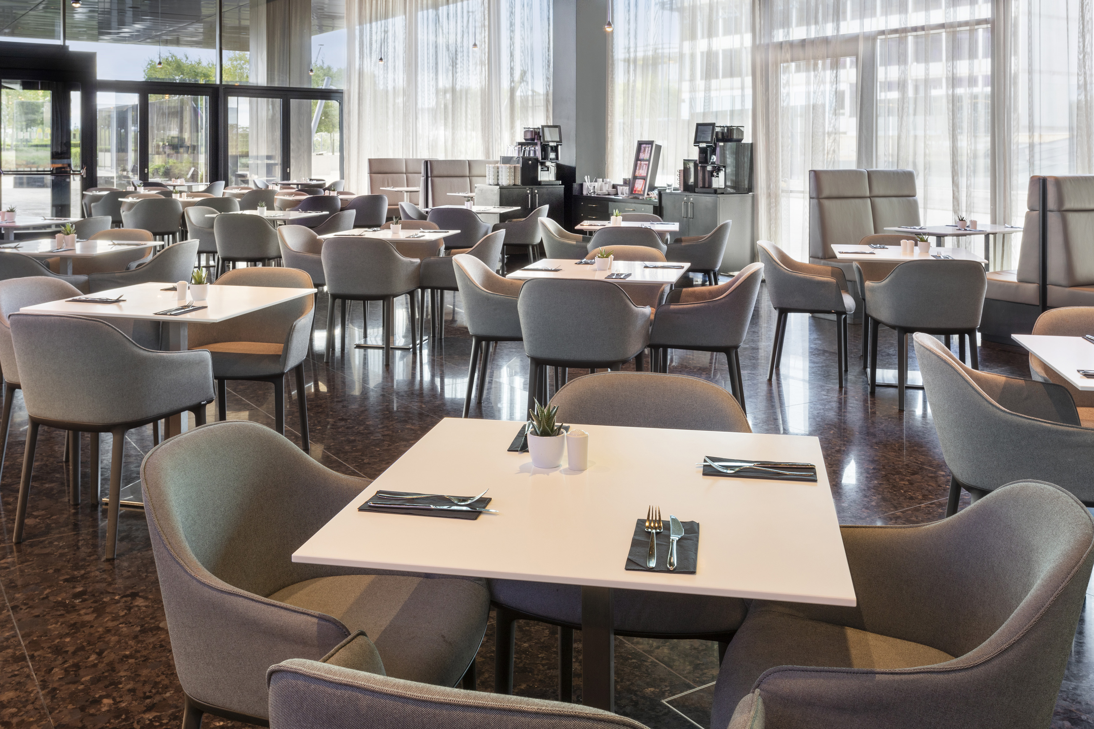 Spacious modern restaurant interior with grey chairs, white tables, and large windows.