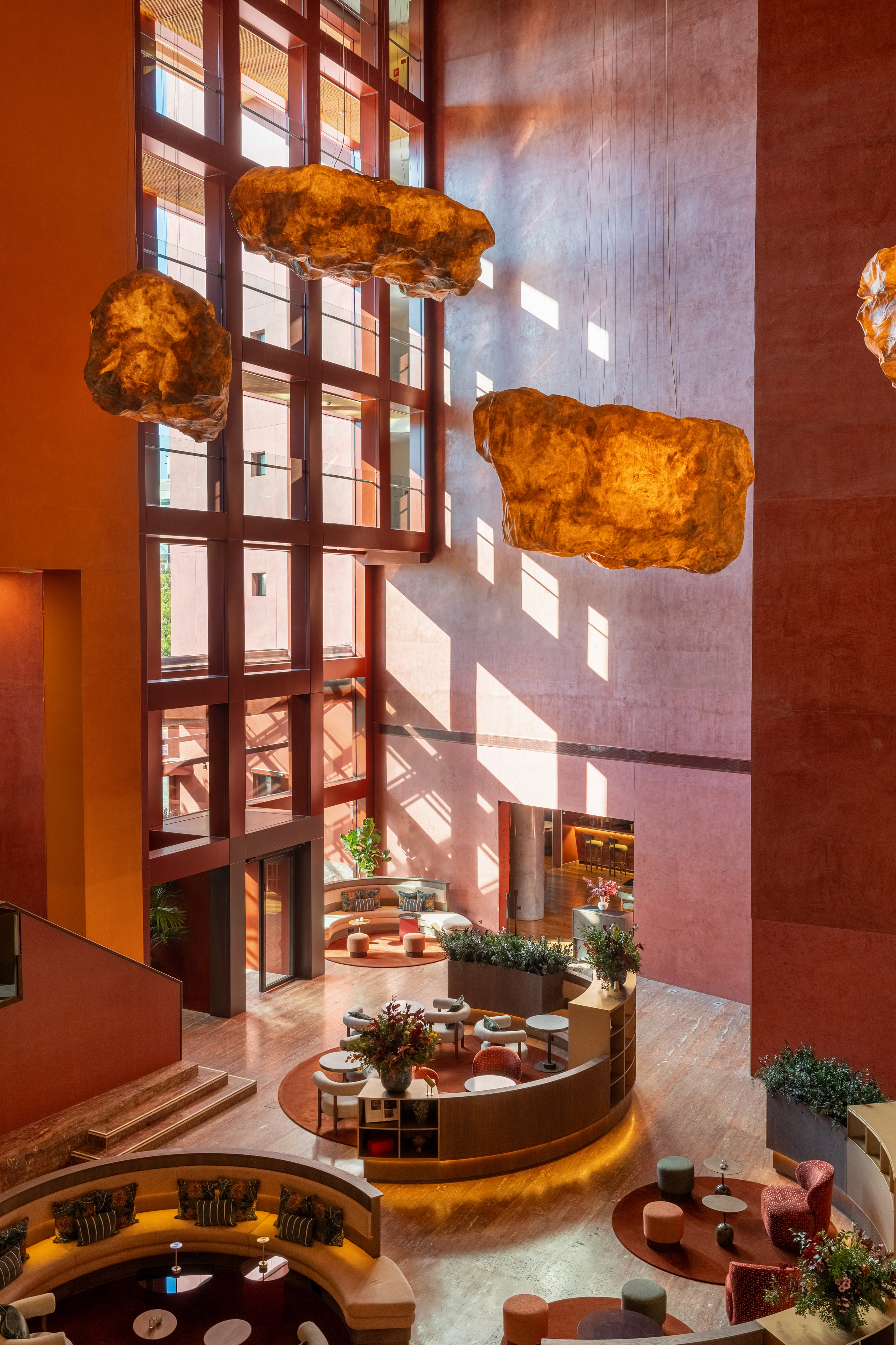 High-ceiling modern hotel lobby, warm terracotta, glowing sculptural lighting.