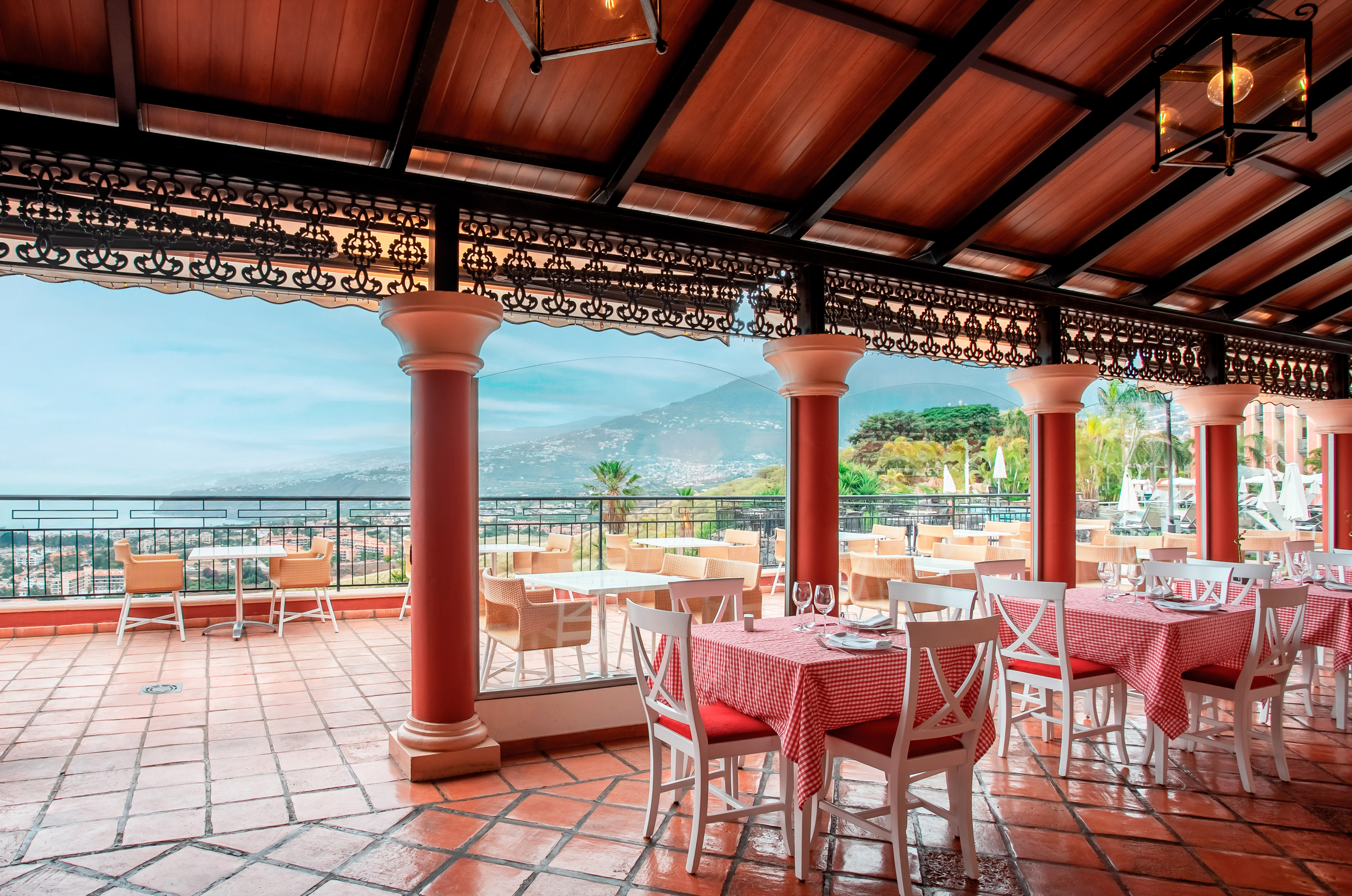 Hotel dining terrace with checkered tables and panoramic mountain-sea view.