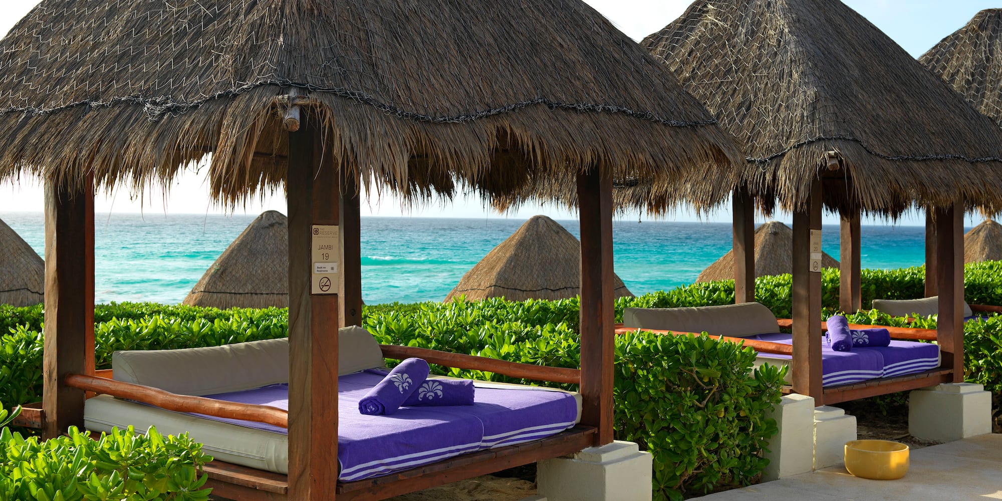 a group of beds with straw roof and a beach in the background