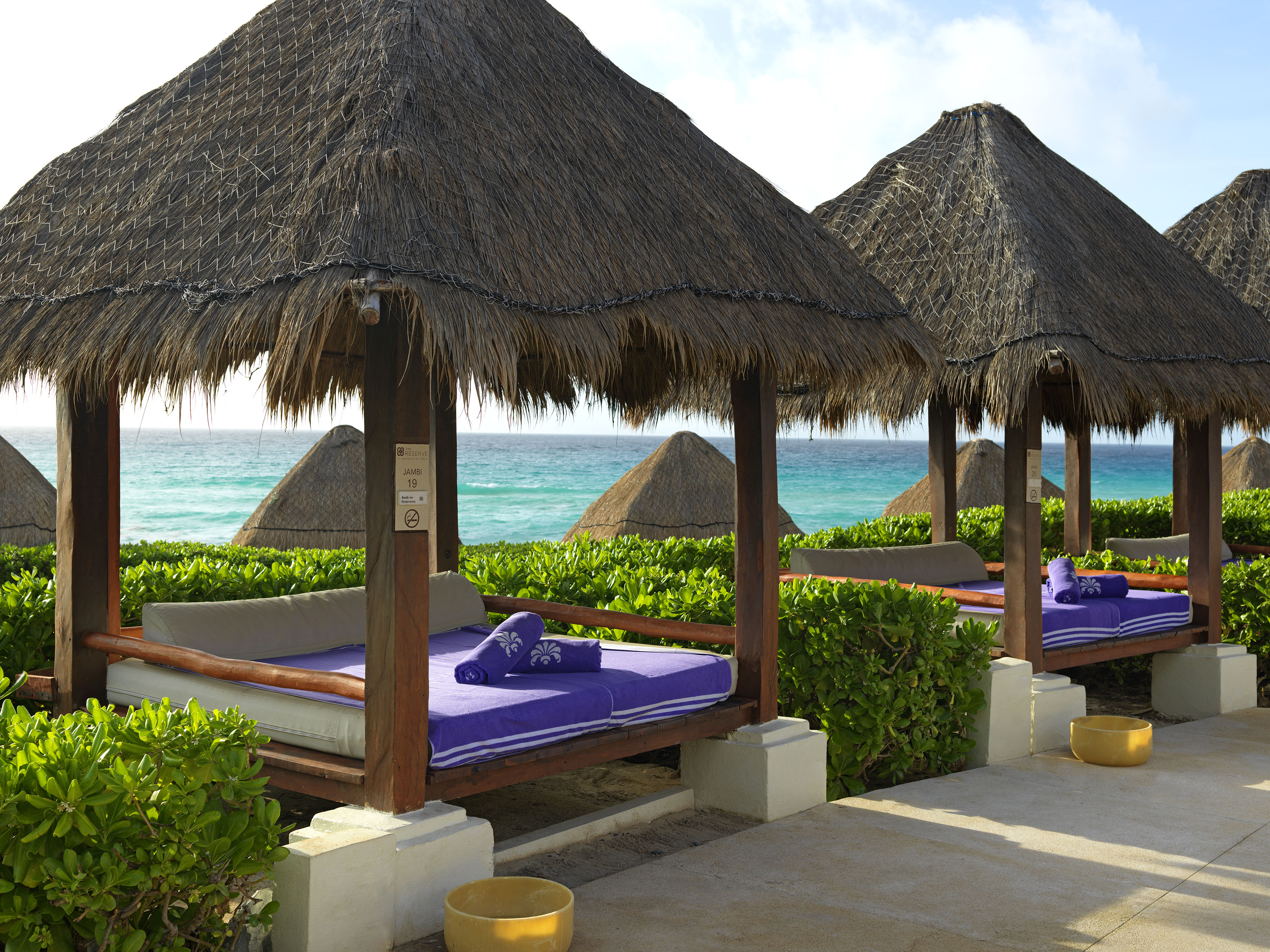 a group of beds with straw roof and a beach in the background