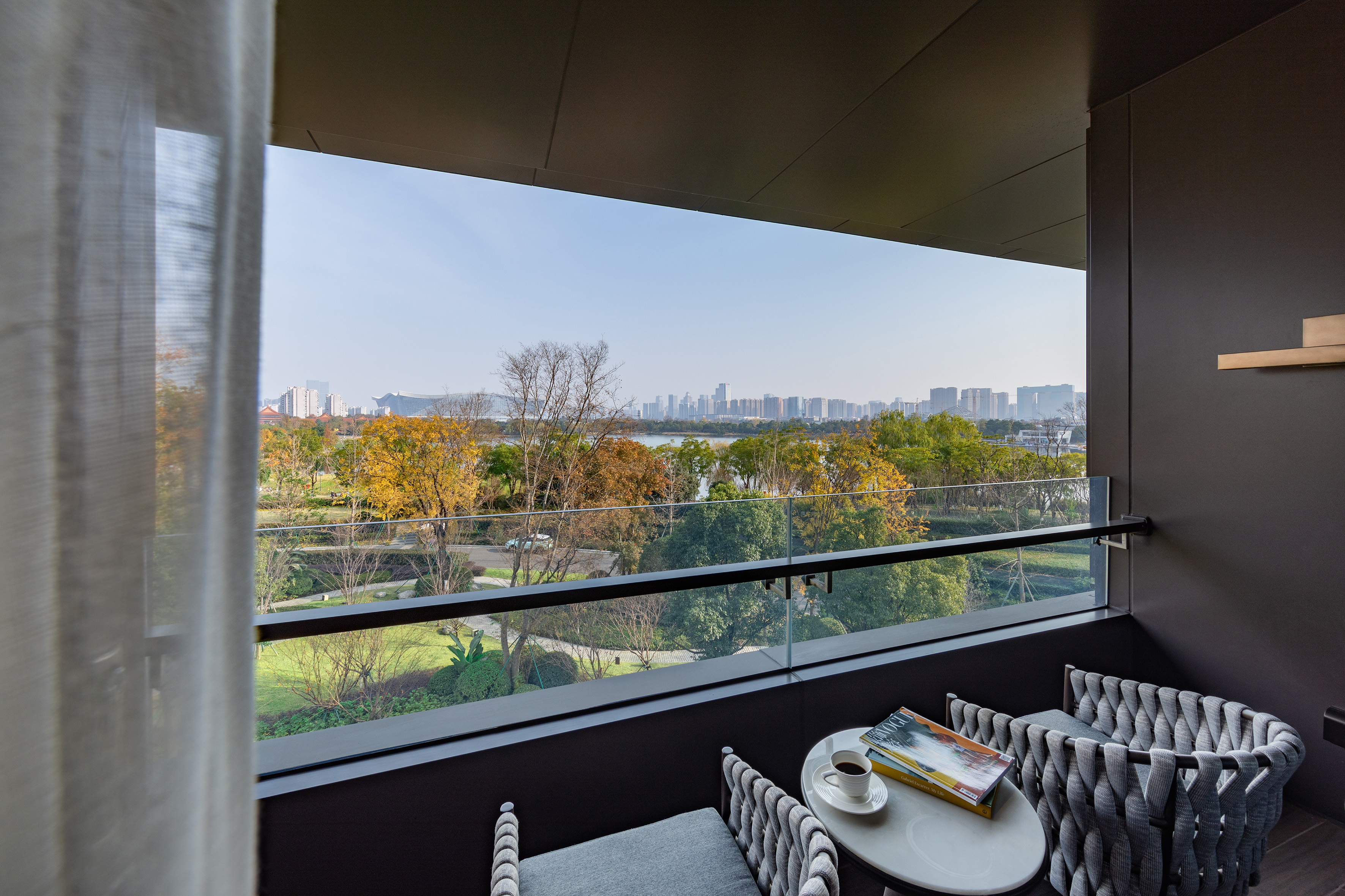 Modern balcony overlooking autumn park, lake, and distant city skyline.