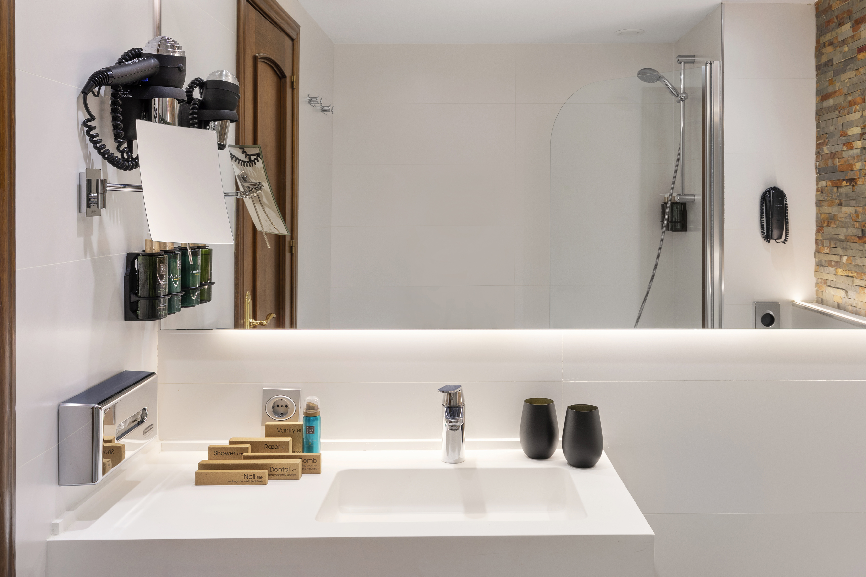 White bathroom vanity with backlit mirror, sink, hairdryer, and hotel amenities.