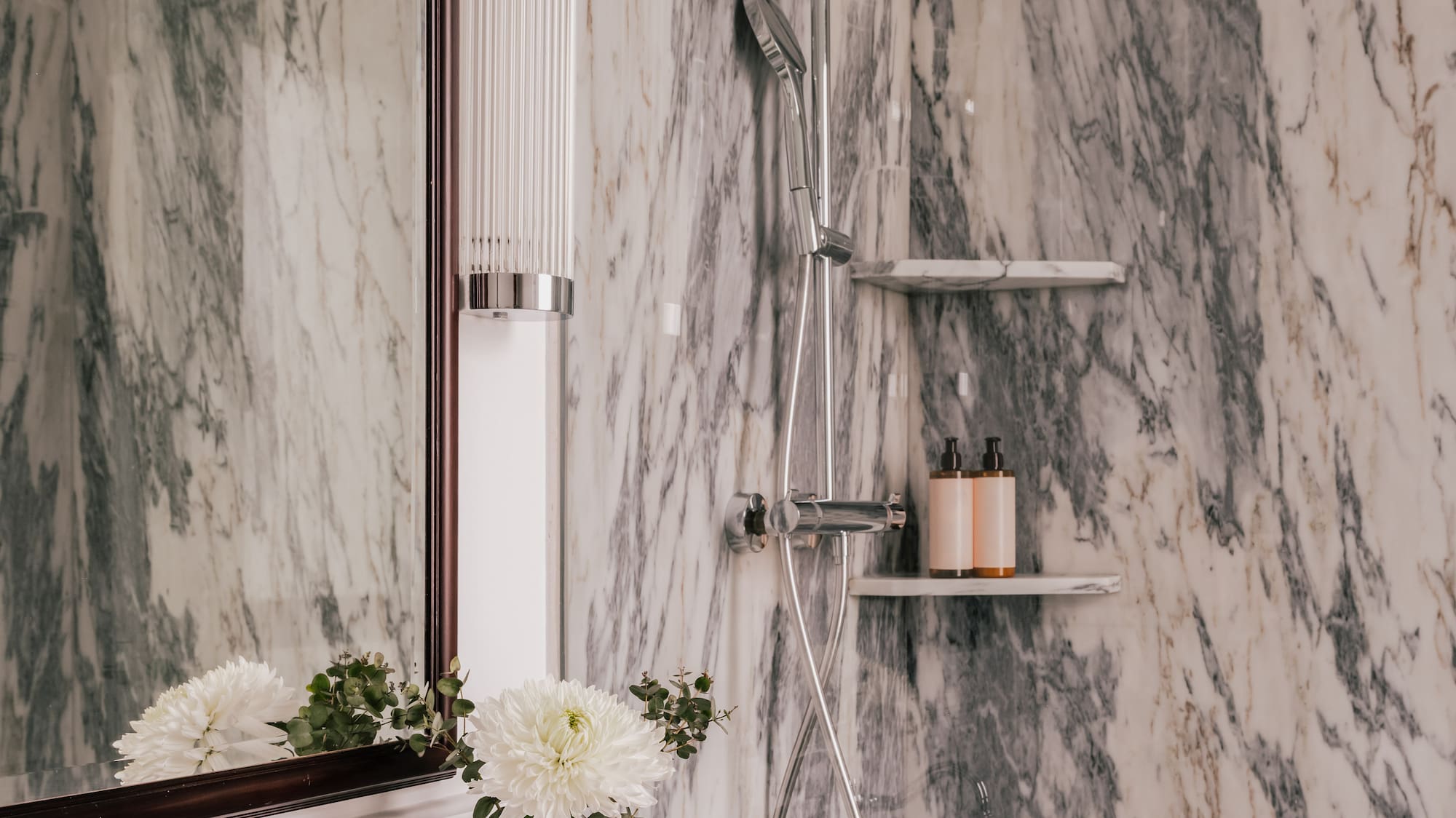 Luxurious marble bathroom with chrome shower, vanity, sink, and decorative flowers.