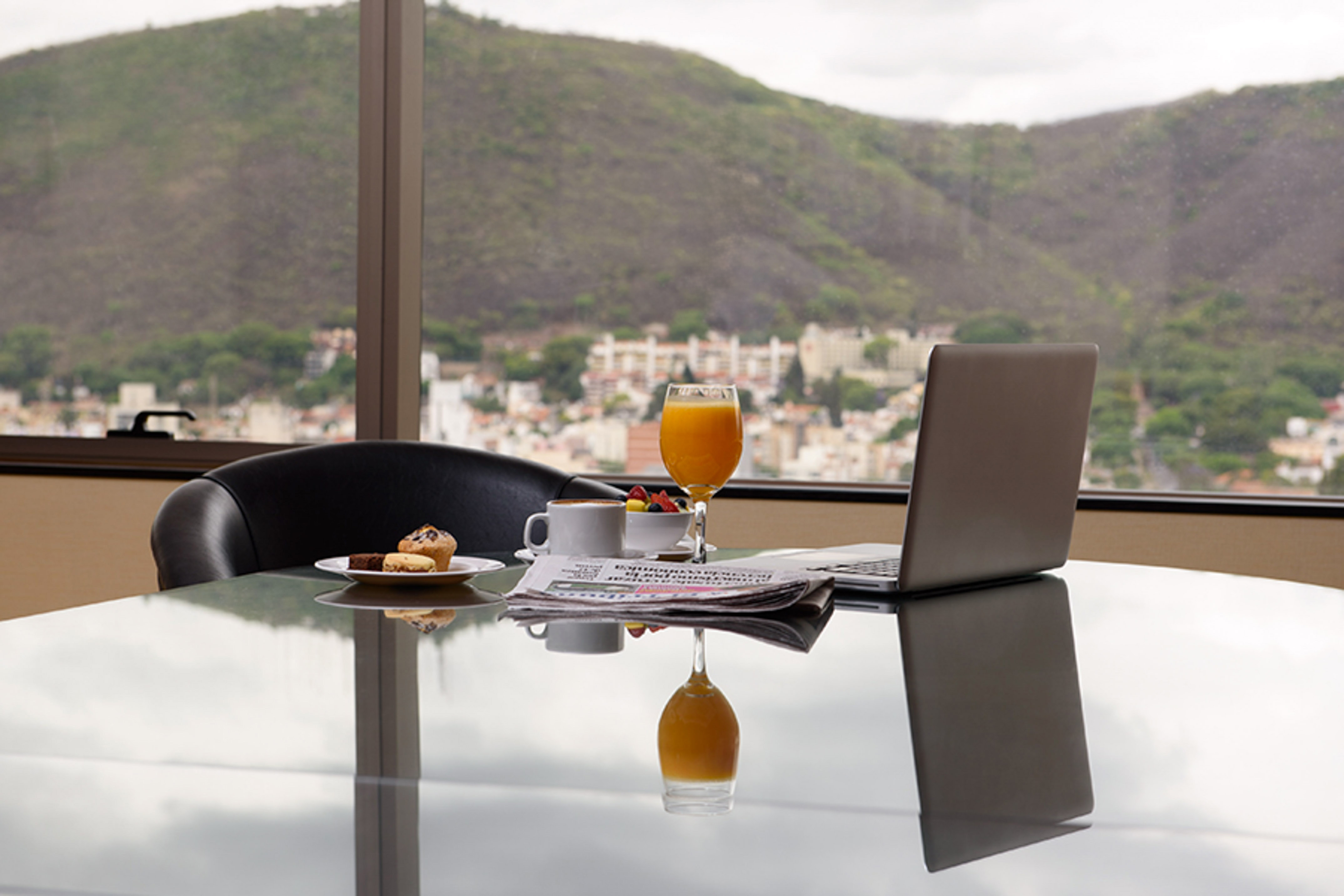 Breakfast with laptop, coffee, juice, and scenic mountain city view.
